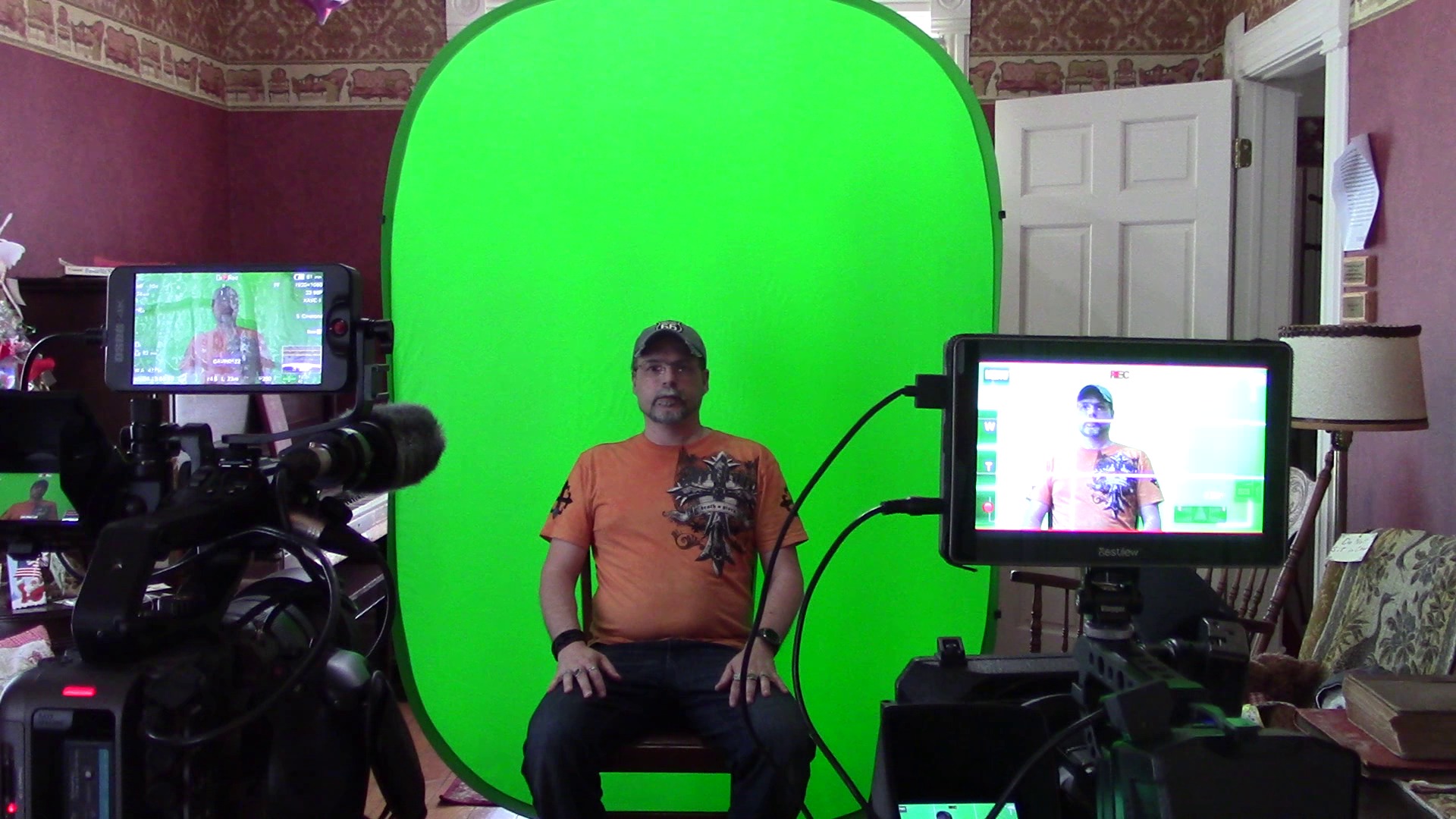 Person sitting in front of a green screen with cameras and monitors around, filming a video.