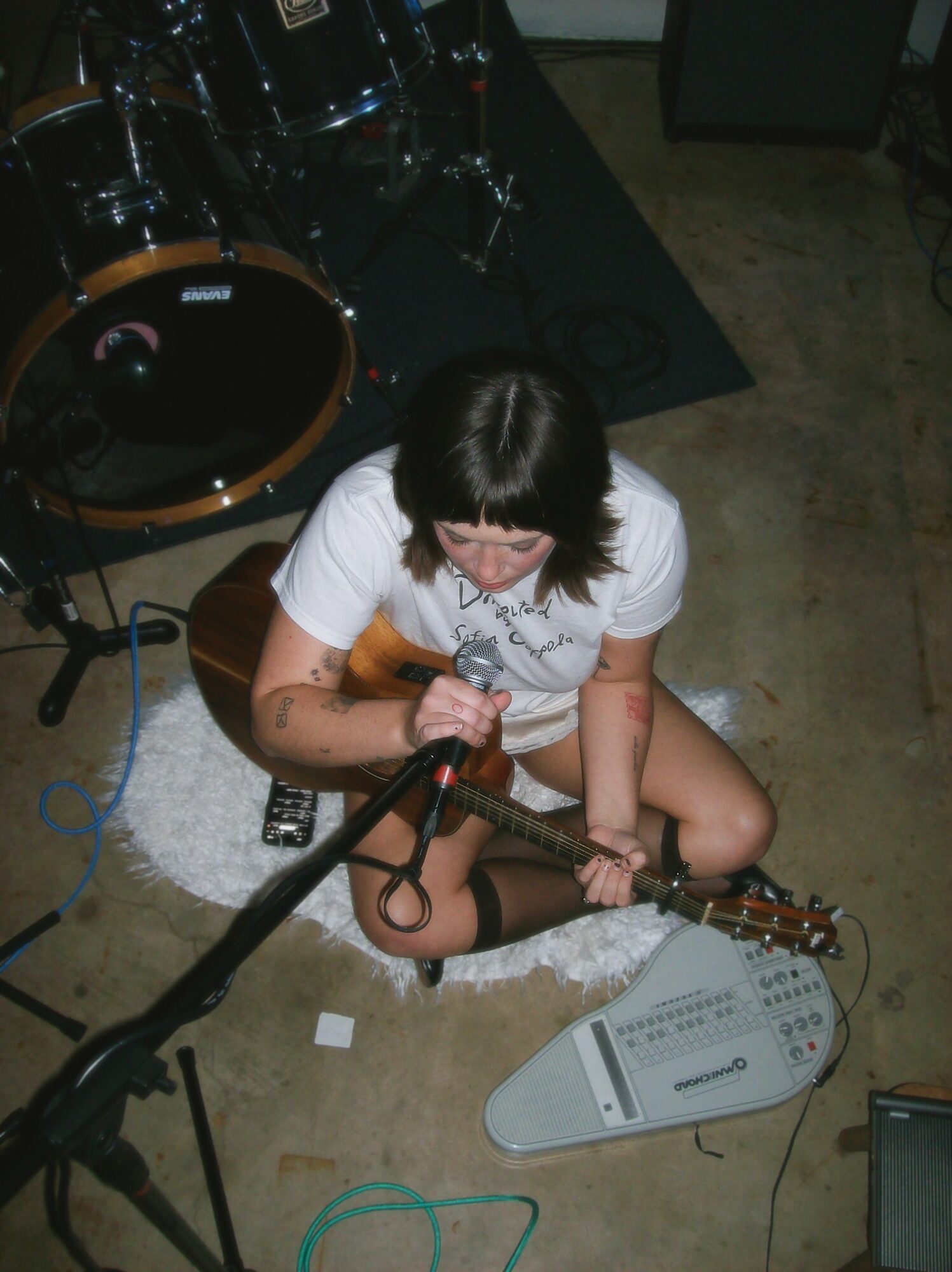 Person sitting on the floor playing guitar, surrounded by musical equipment, viewed from above.
