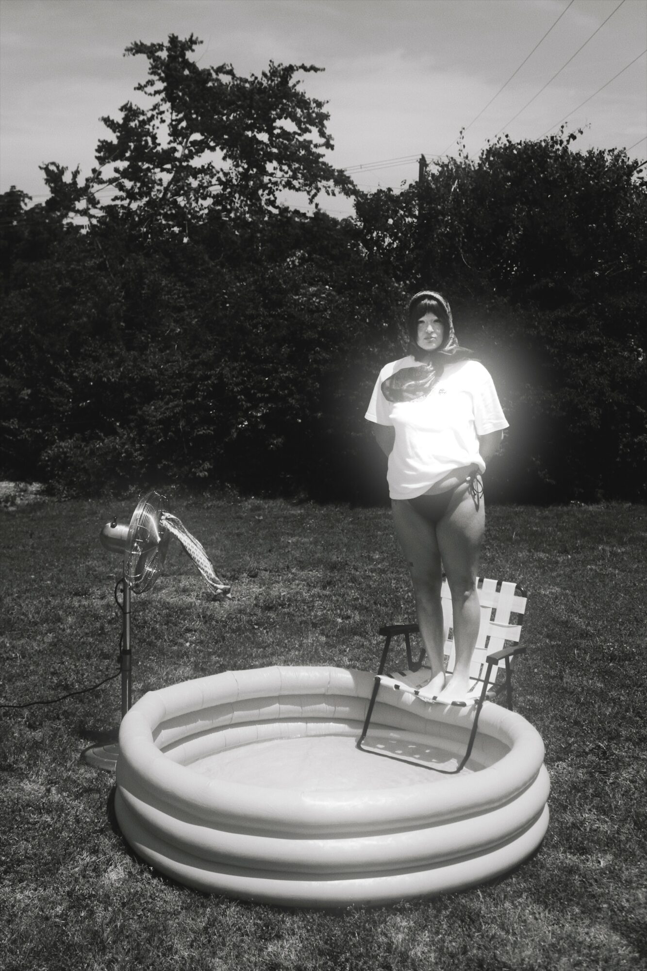 Person standing in a small inflatable pool outdoors, with trees and sky in the background.