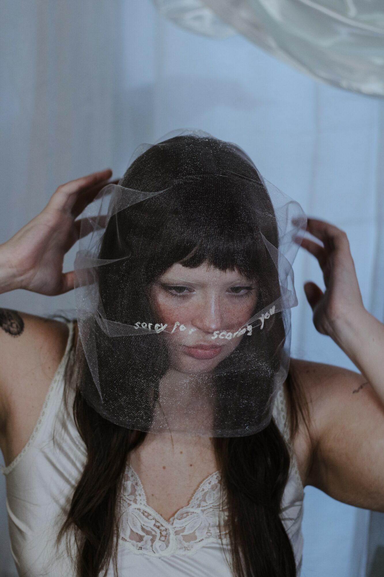 Young woman with long dark hair wears a transparent face shield, adjusting it with both hands, against a light background.