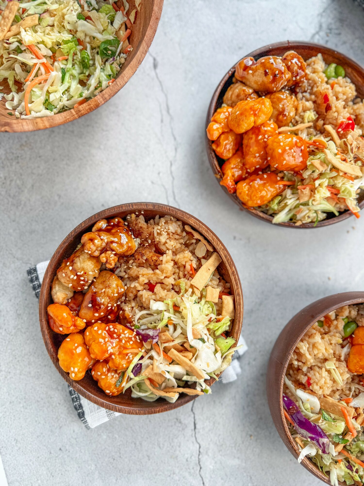 Three bowls of Asian-inspired dishes with rice, vegetables, and fried chicken on a light surface.