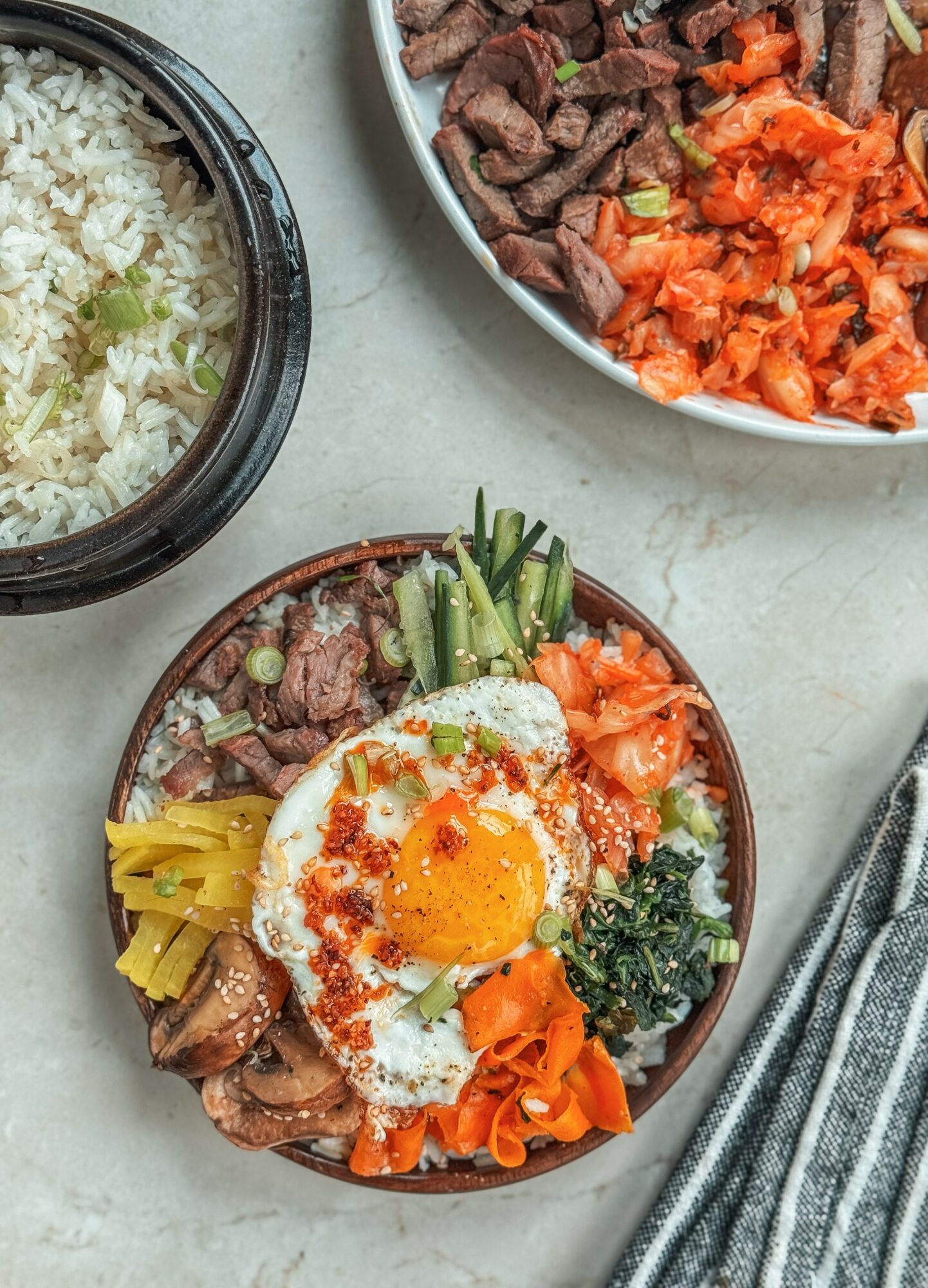 Bowl with rice, cooked beef, vegetables, and a fried egg on top, garnished with green onions and spices.