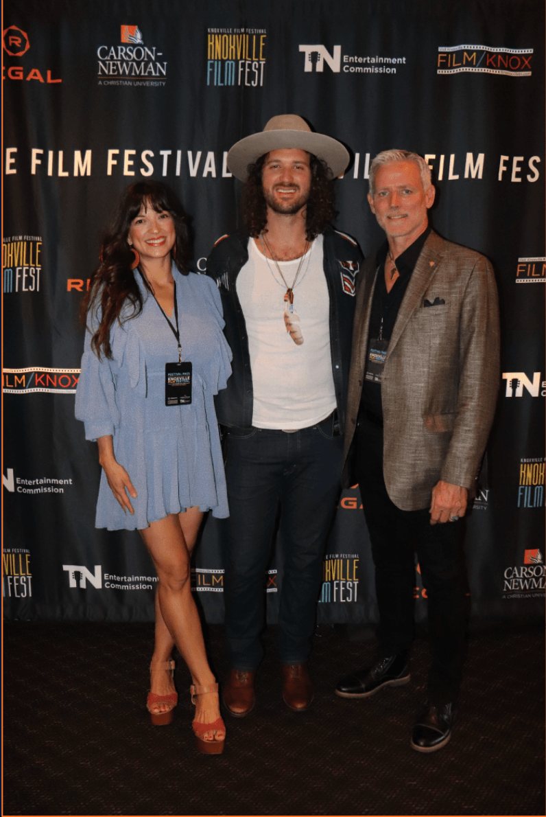 Three people standing together at a film festival, smiling, with a black backdrop featuring festival logos.