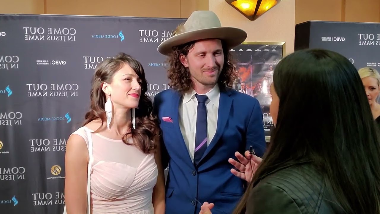 Three people engaged in conversation at an event, with a backdrop displaying text and images.