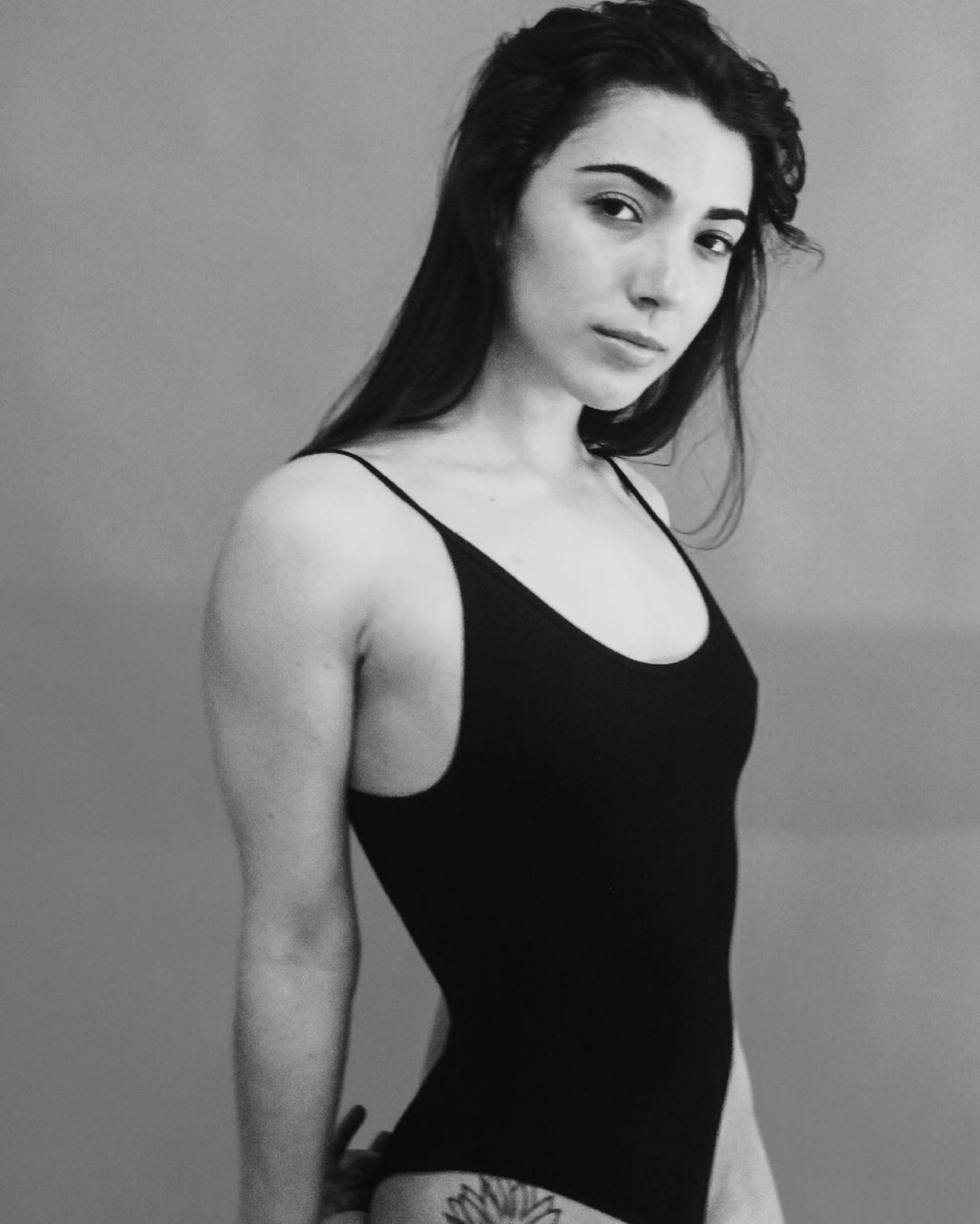 Young woman with long dark hair in a black sleeveless top, looking at the camera, plain background.