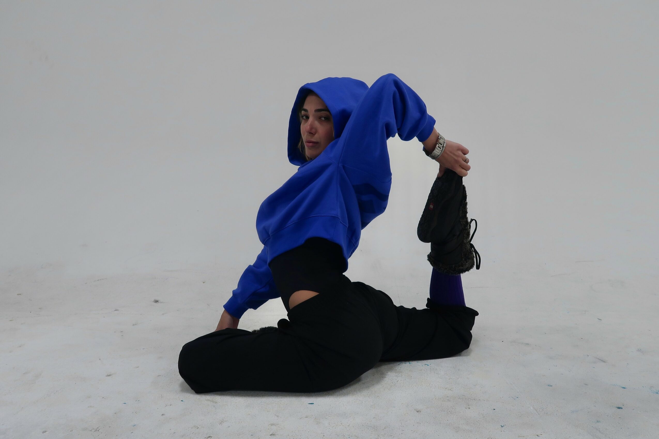 Person in blue hoodie performing a yoga pose on a plain white background.