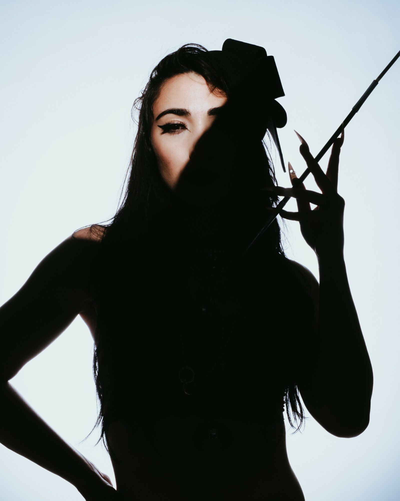 Silhouette of a woman holding a cigarette holder, with one eye visible, against a light background.