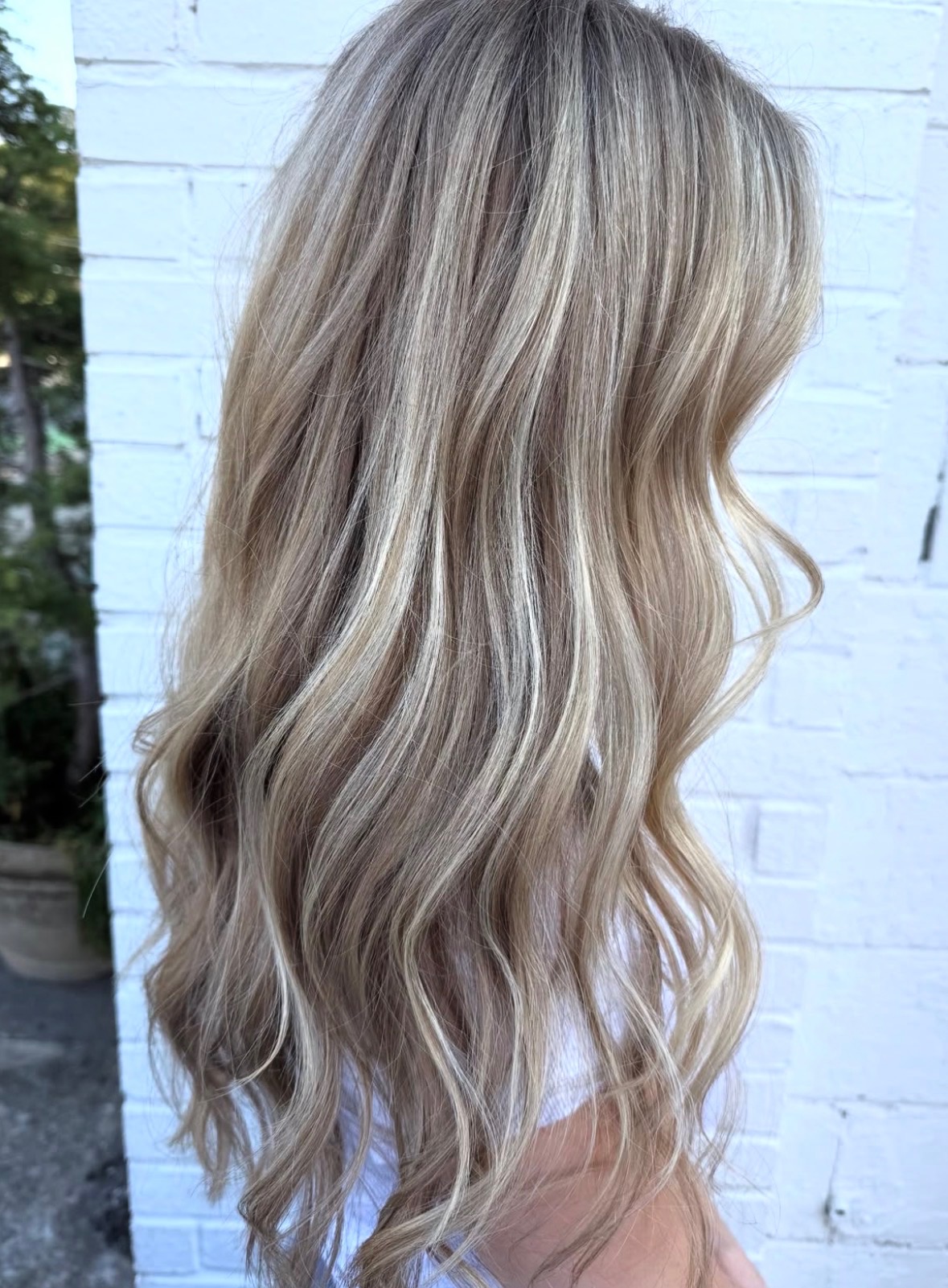 Side view of long, wavy blonde hair against a white brick wall.