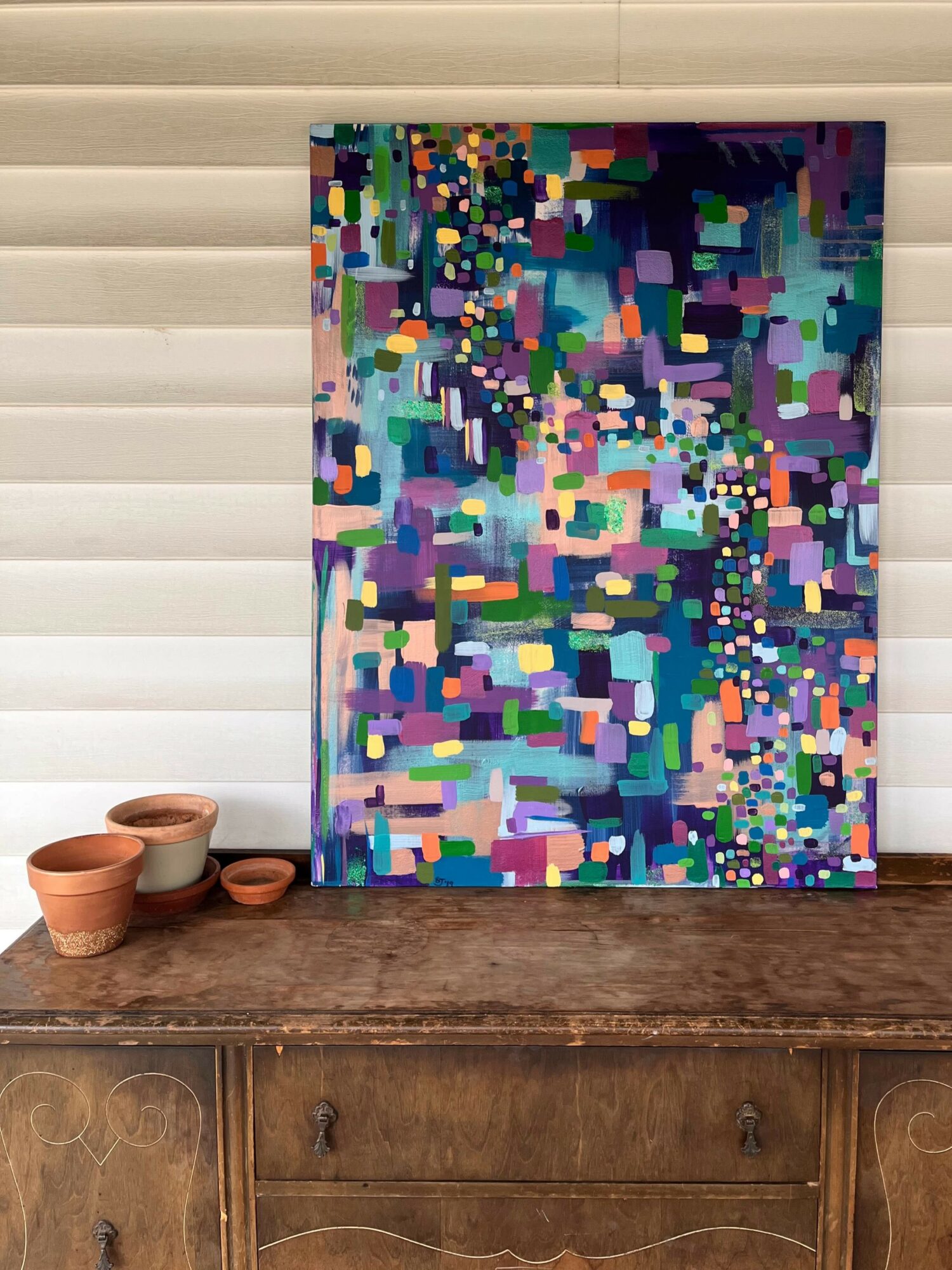 Colorful abstract painting with various shapes and patterns leaning against a wall on a wooden surface.