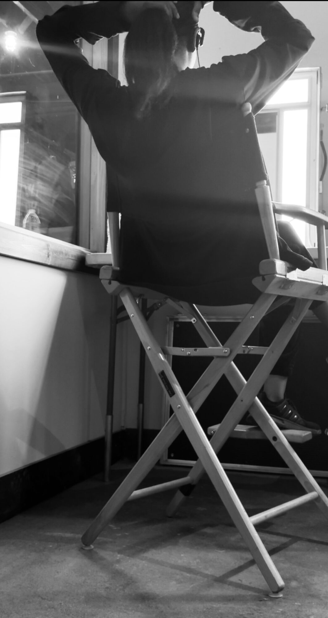 Person sitting on a chair with arms raised, back facing window, in a room with a desk and window.