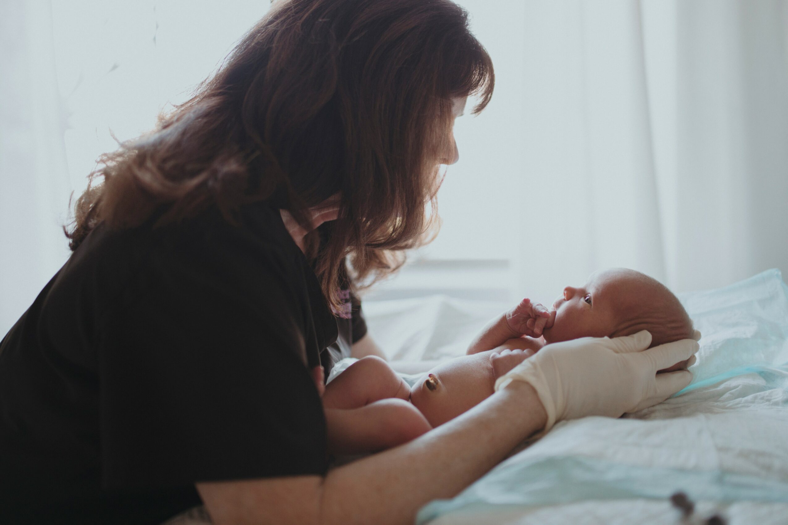 Woman holding a newborn baby on a bed, with soft natural light in the background.