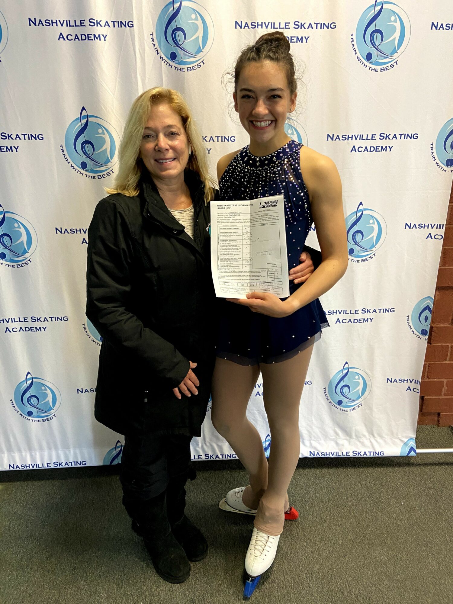 Two people, a woman and a young girl, stand together holding a certificate at Nashville Skating Academy. They smile for the photo.