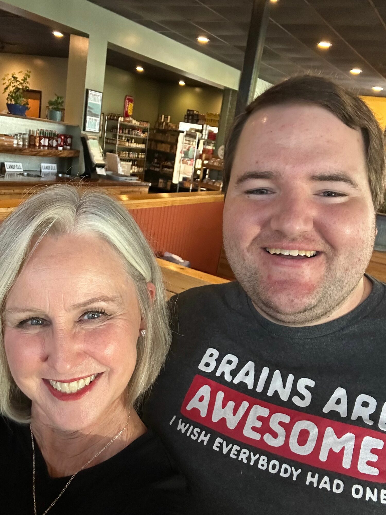 Two smiling people, a man with dark hair and a woman with white hair, in a restaurant setting.