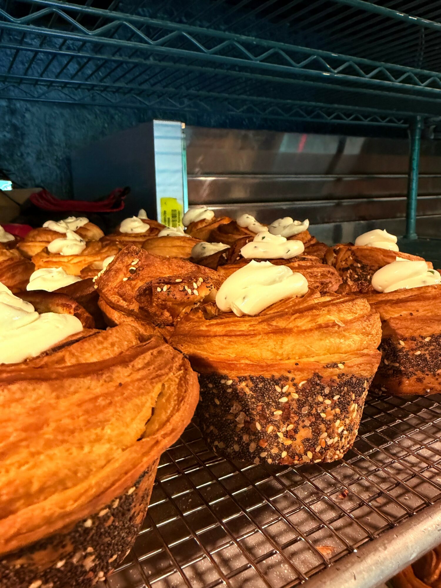 Several muffins with white icing and nuts on top are displayed on a wire rack in a bakery setting.