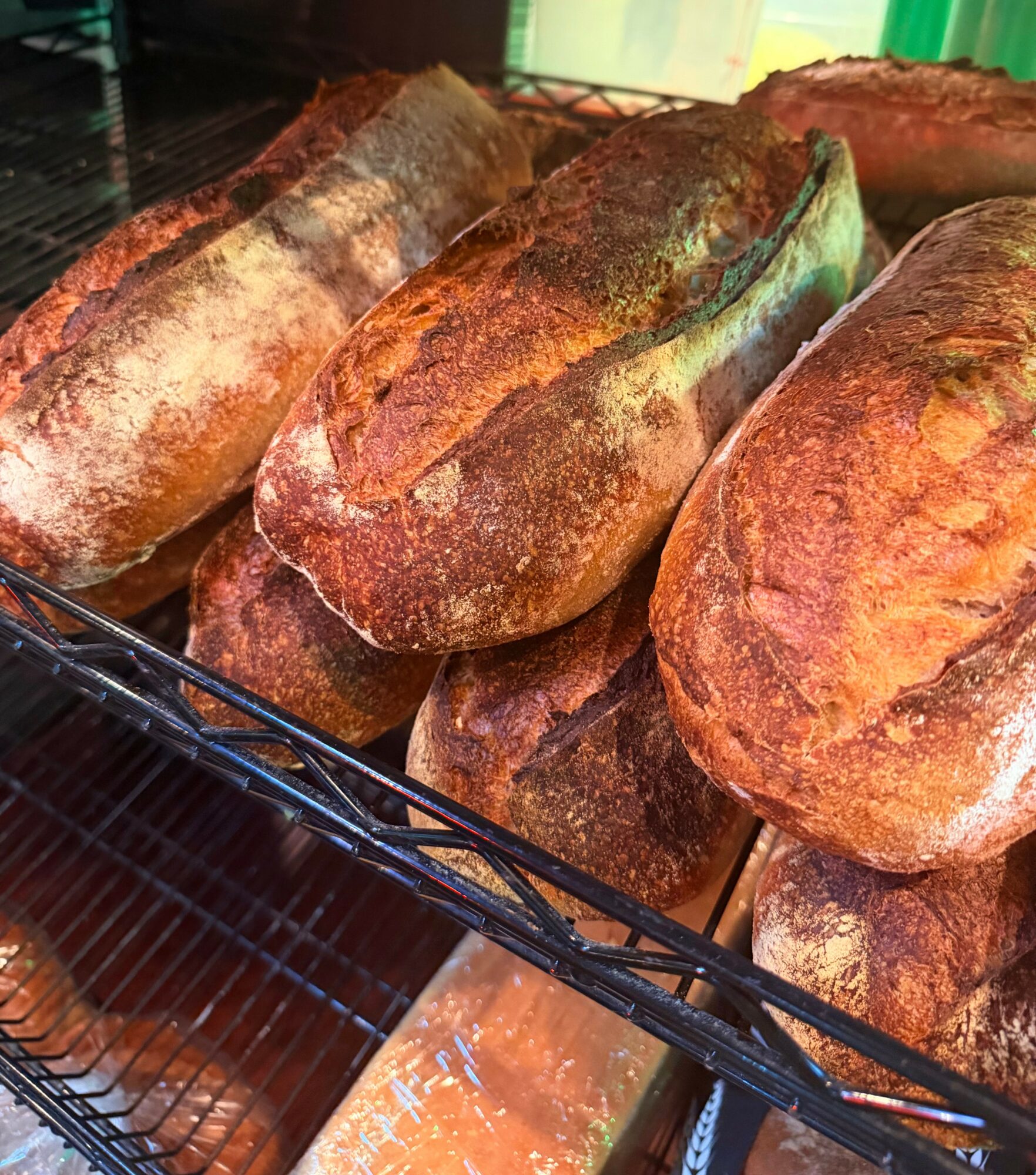 Loaves of bread stacked on a wire rack, with a crusty appearance and golden-brown color.