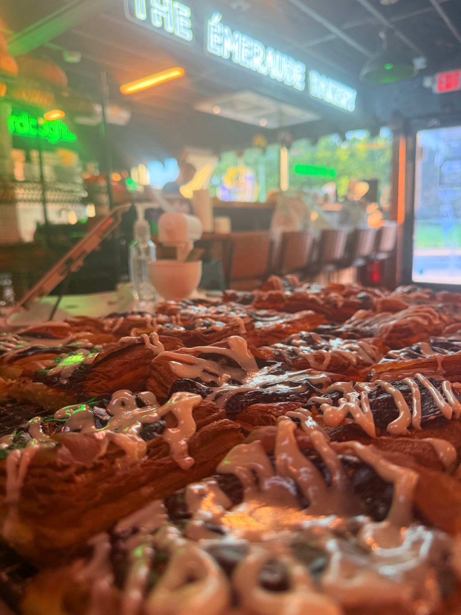 Close-up of assorted cookies with icing and chocolate, inside a lively cafe or restaurant with neon signs and seating in the background.