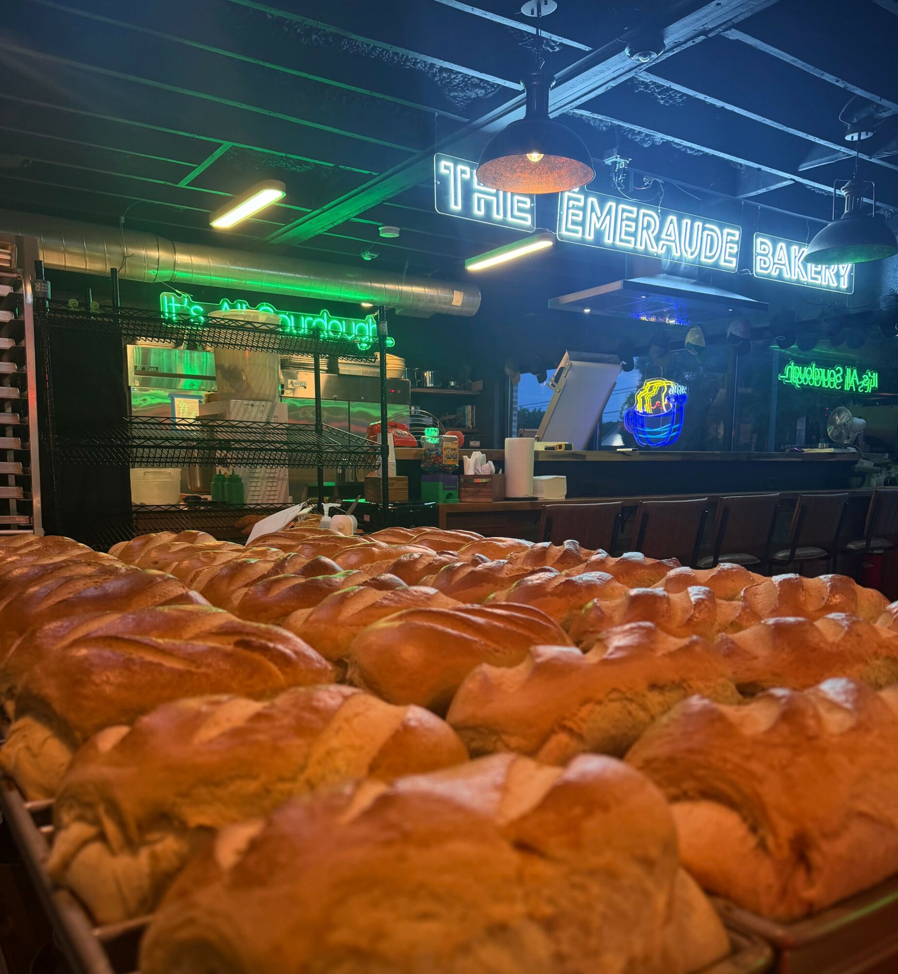 Tray of croissants in front of a bar with neon signs and a dark ceiling, illuminated by green and blue lights.