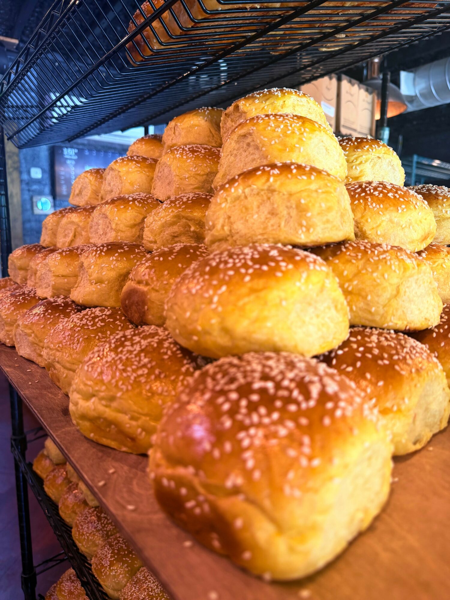 Stack of golden-brown bread rolls sprinkled with salt on a wooden surface in a bakery.