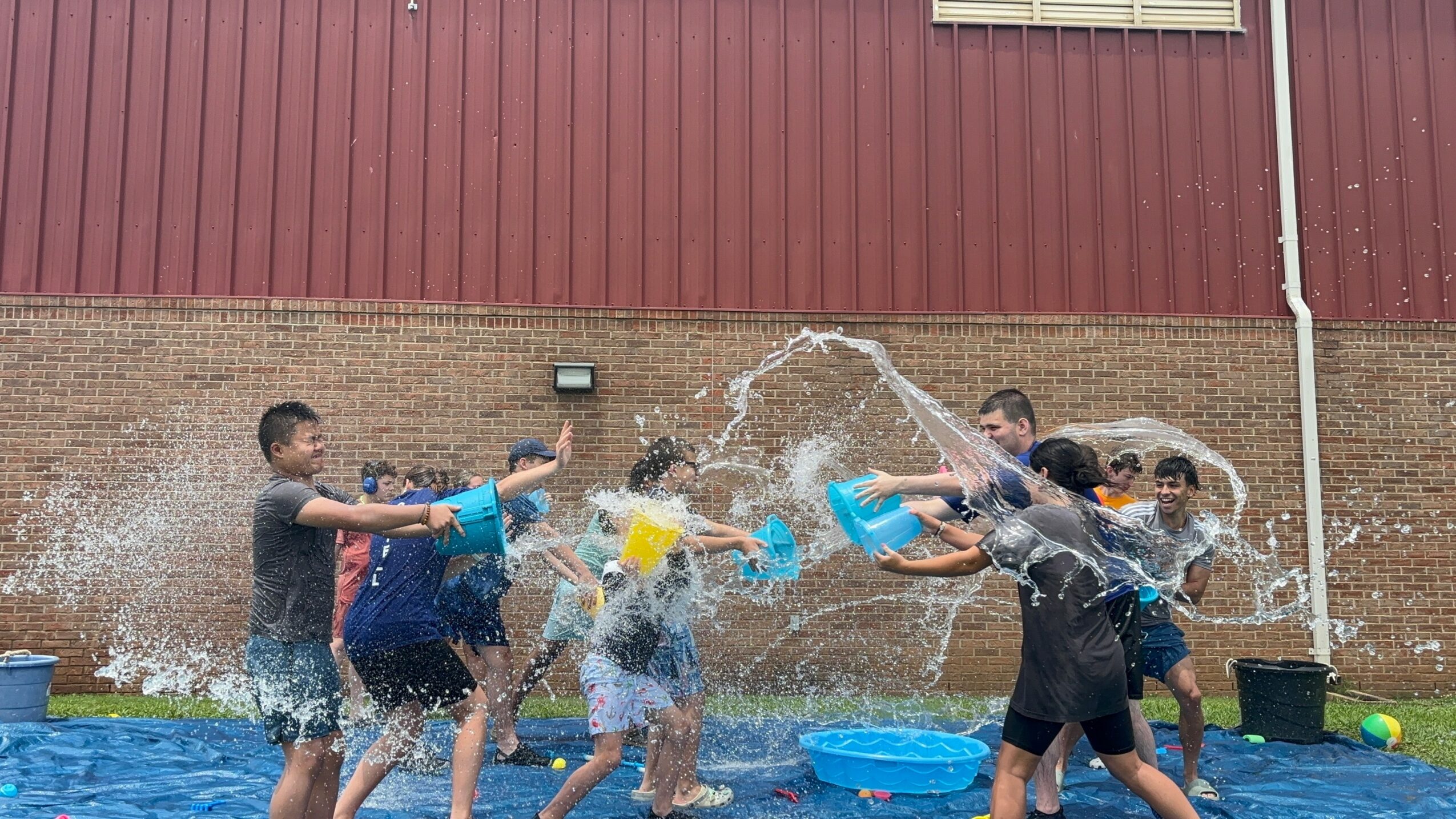 Children playing with water buckets outdoors, splashing water, and having fun.