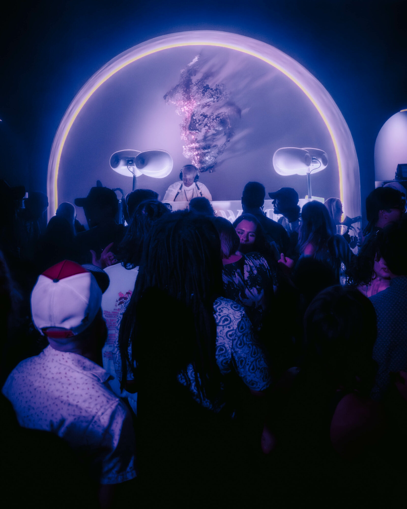 Crowd of people in a dark room with a large circular screen displaying a lion's face and a glowing halo, with two illuminated objects on either side.
