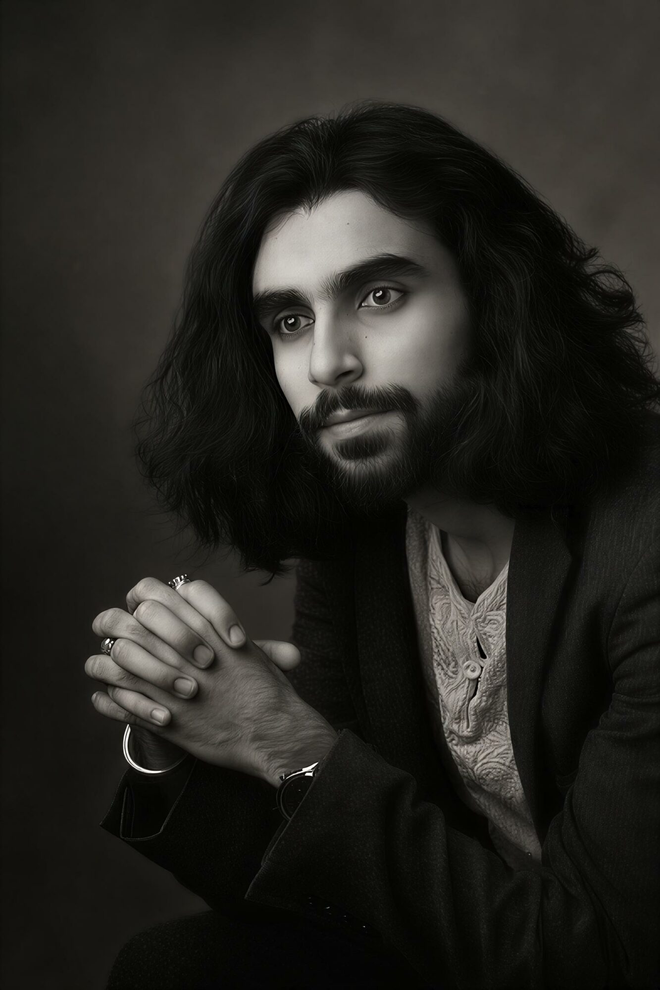 Portrait of a person with long, wavy hair, looking to the side, hands clasped, in black and white.