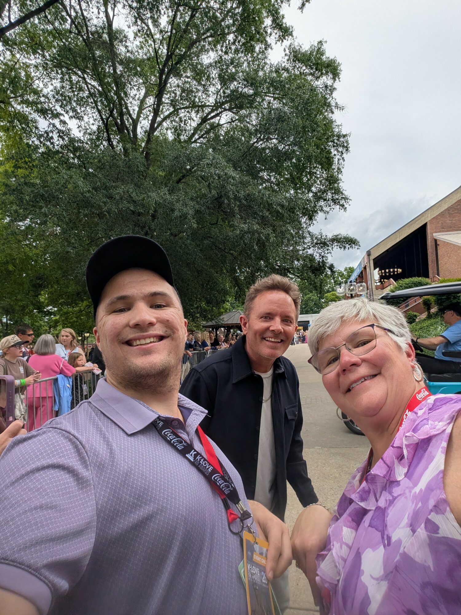 Three people smiling outdoors, with trees and a building in the background.
