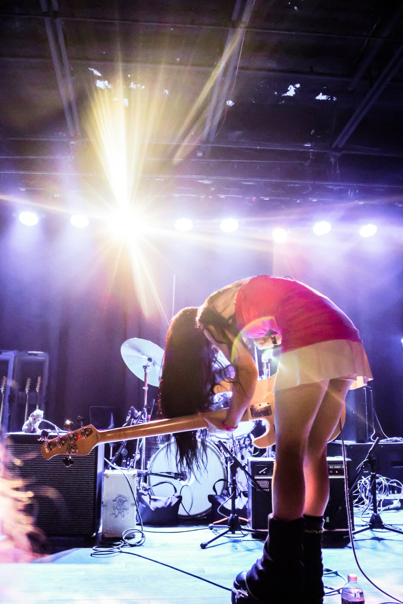 Two people on stage, one bending over, with bright stage lights overhead and musical equipment around them.
