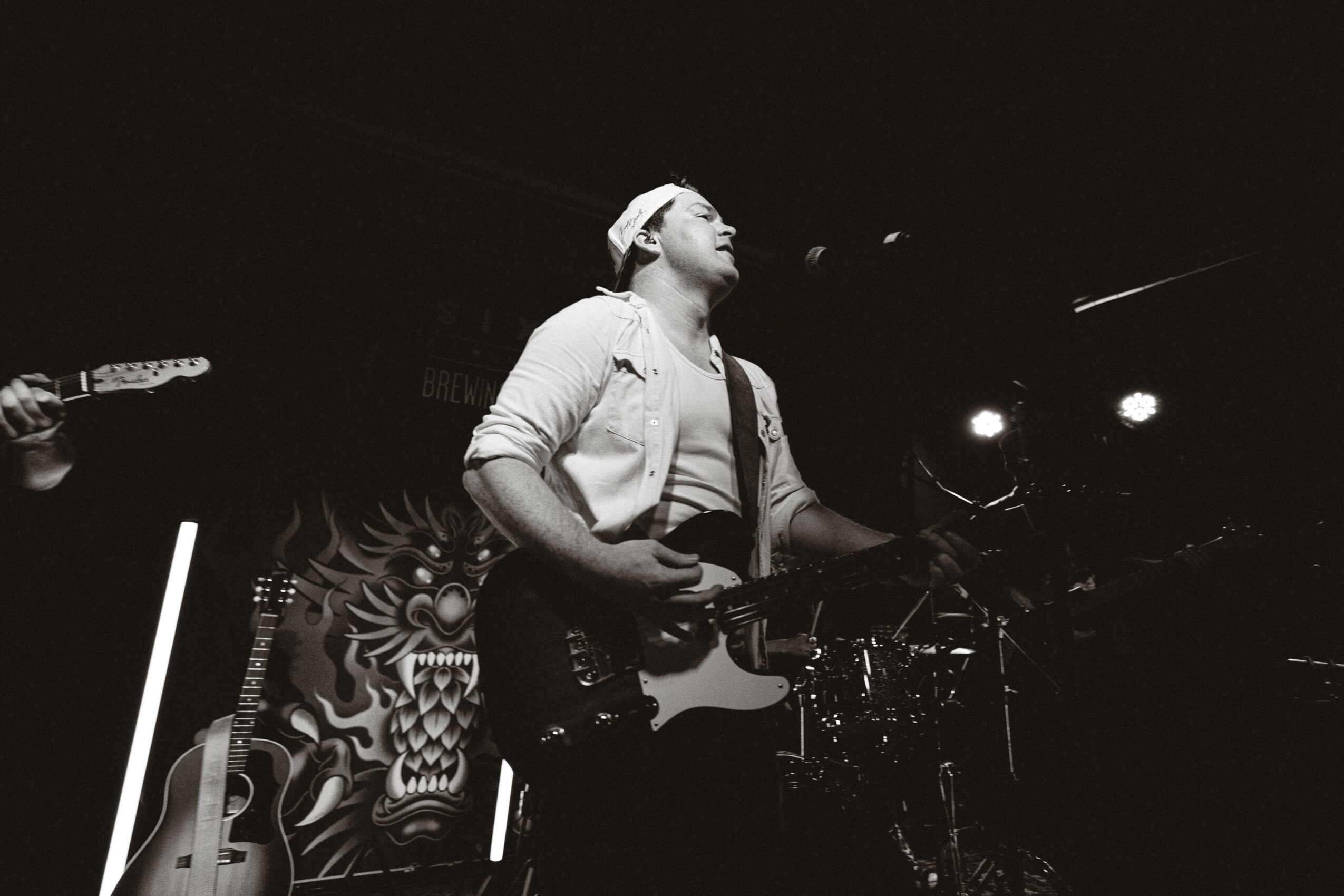 Person playing guitar on stage with a patterned backdrop, stage lights shining, in black and white.