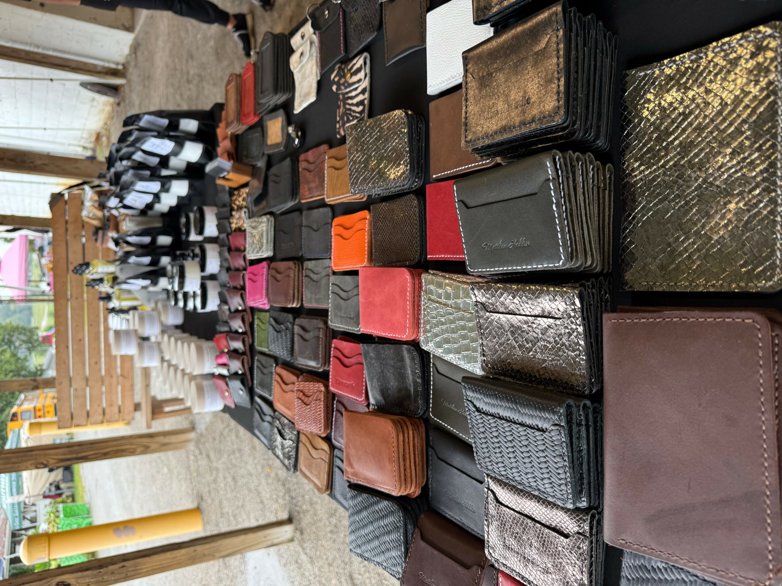 Display of wallets and cardholders arranged on a table outdoors, with various colors and textures.