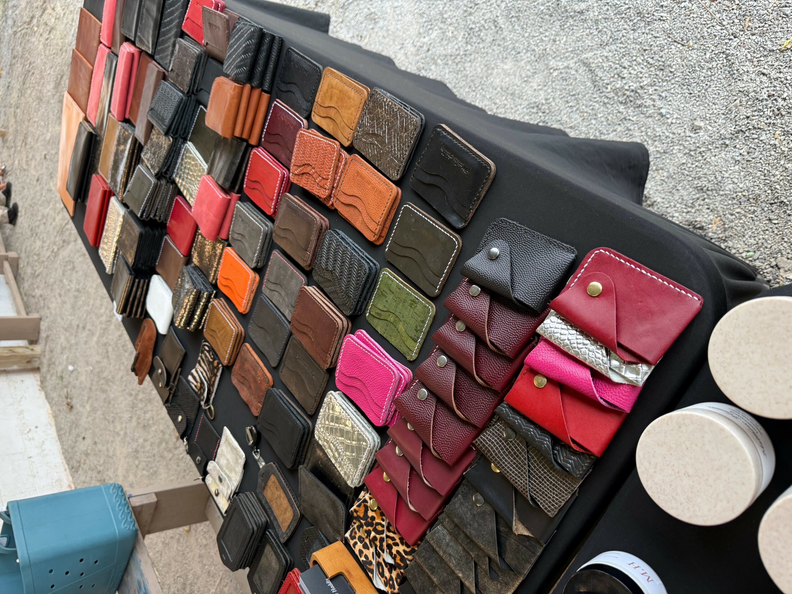 Display of various wallets and pouches arranged on a black surface outdoors.