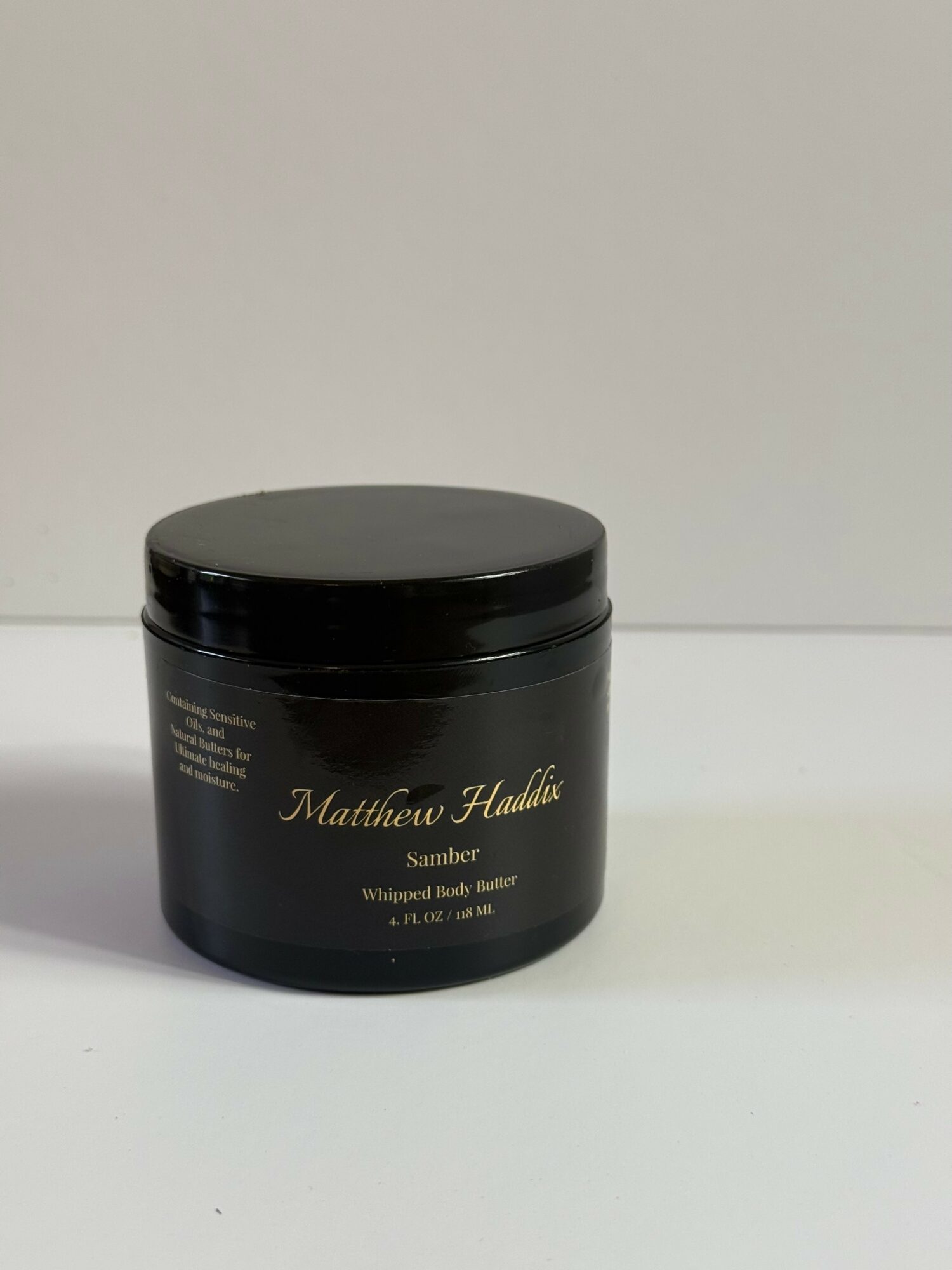 Black jar with gold text on a white surface and background, labeled Matthew Handic Summer whipped body butter, 8 oz.
