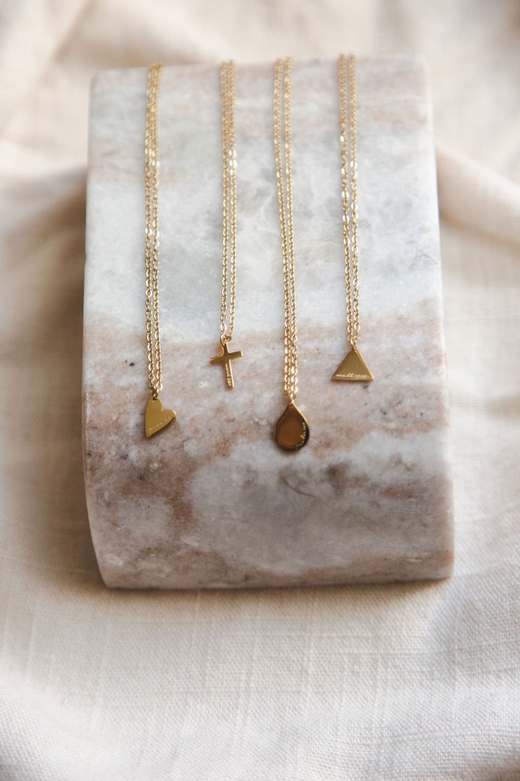 Four gold necklaces with different pendant shapes displayed on a marble stand.