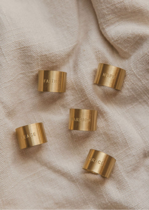 Five gold-colored rings with engraved words placed on a light fabric surface.