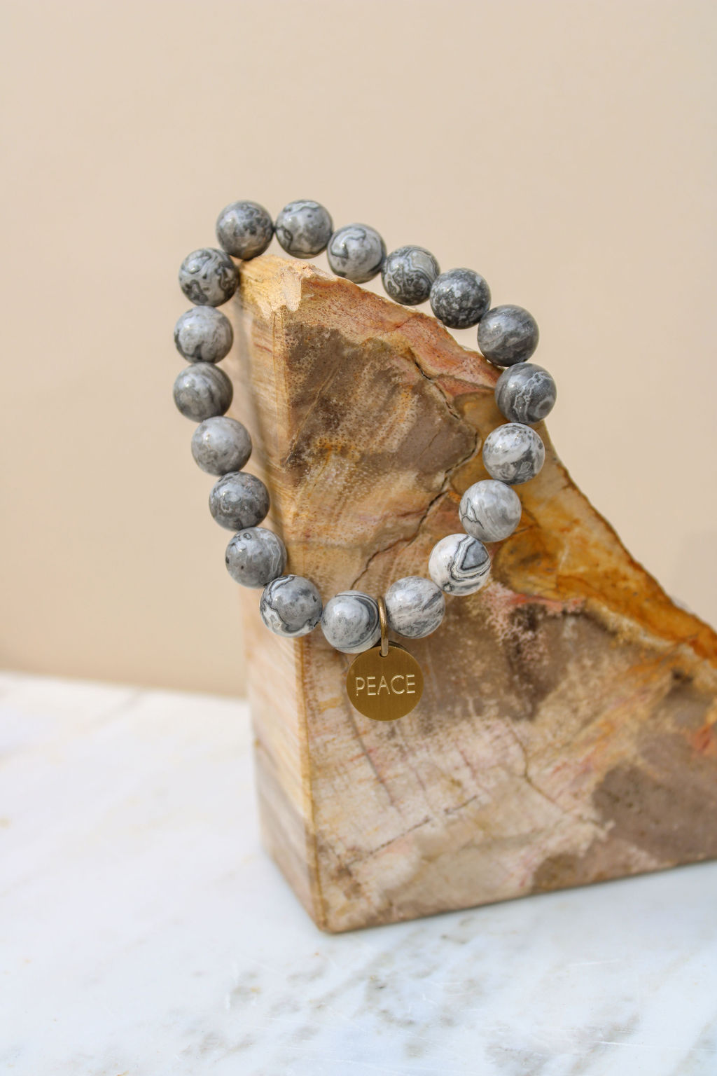 Beaded necklace with a round gold pendant resting on a wooden block, against a plain background.