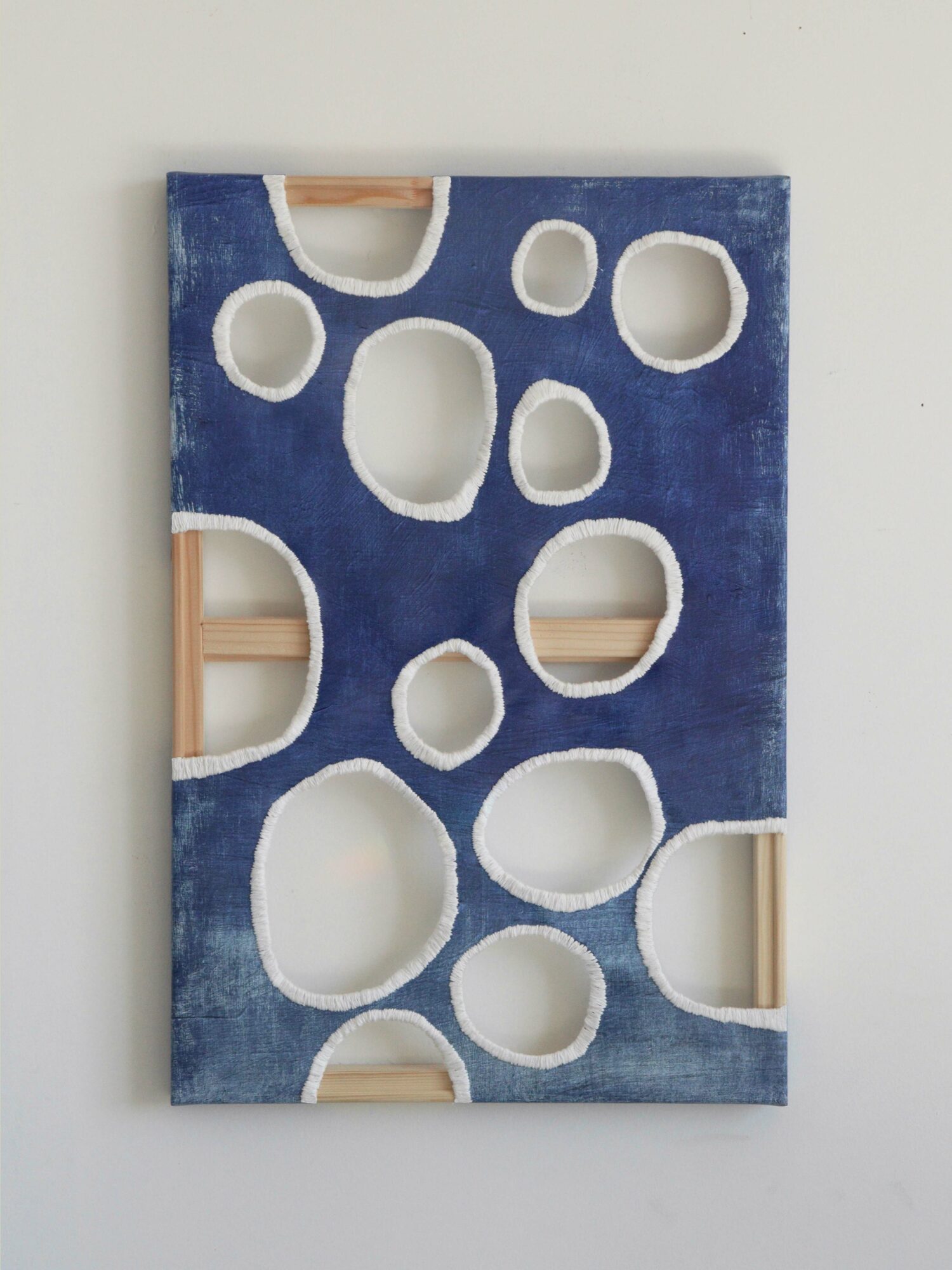 Blue wall art with circular cutouts, mounted on a white wall, with visible wooden supports inside some cutouts.