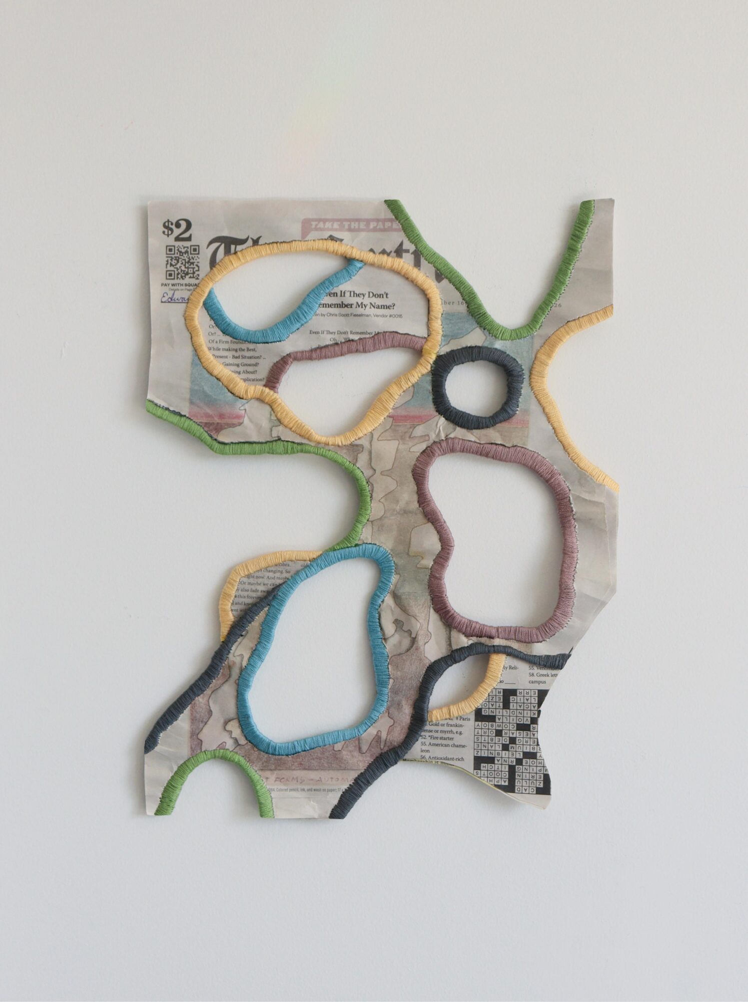 Colorful paper cutouts with embroidered outlines on a newspaper background, arranged on a white surface.