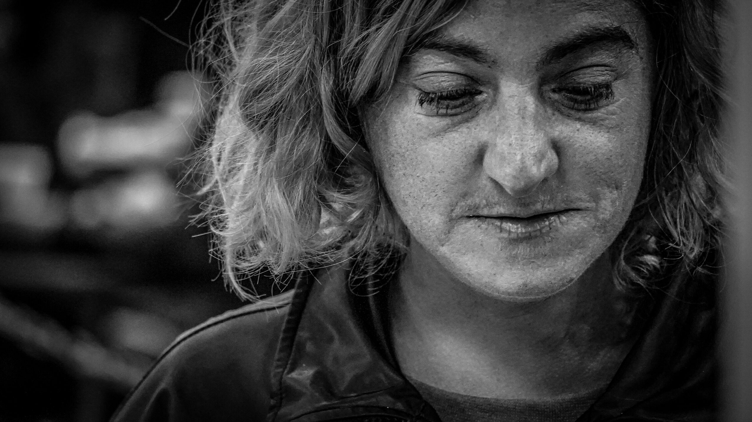 Close-up of a woman with wavy hair looking downward, in black and white.