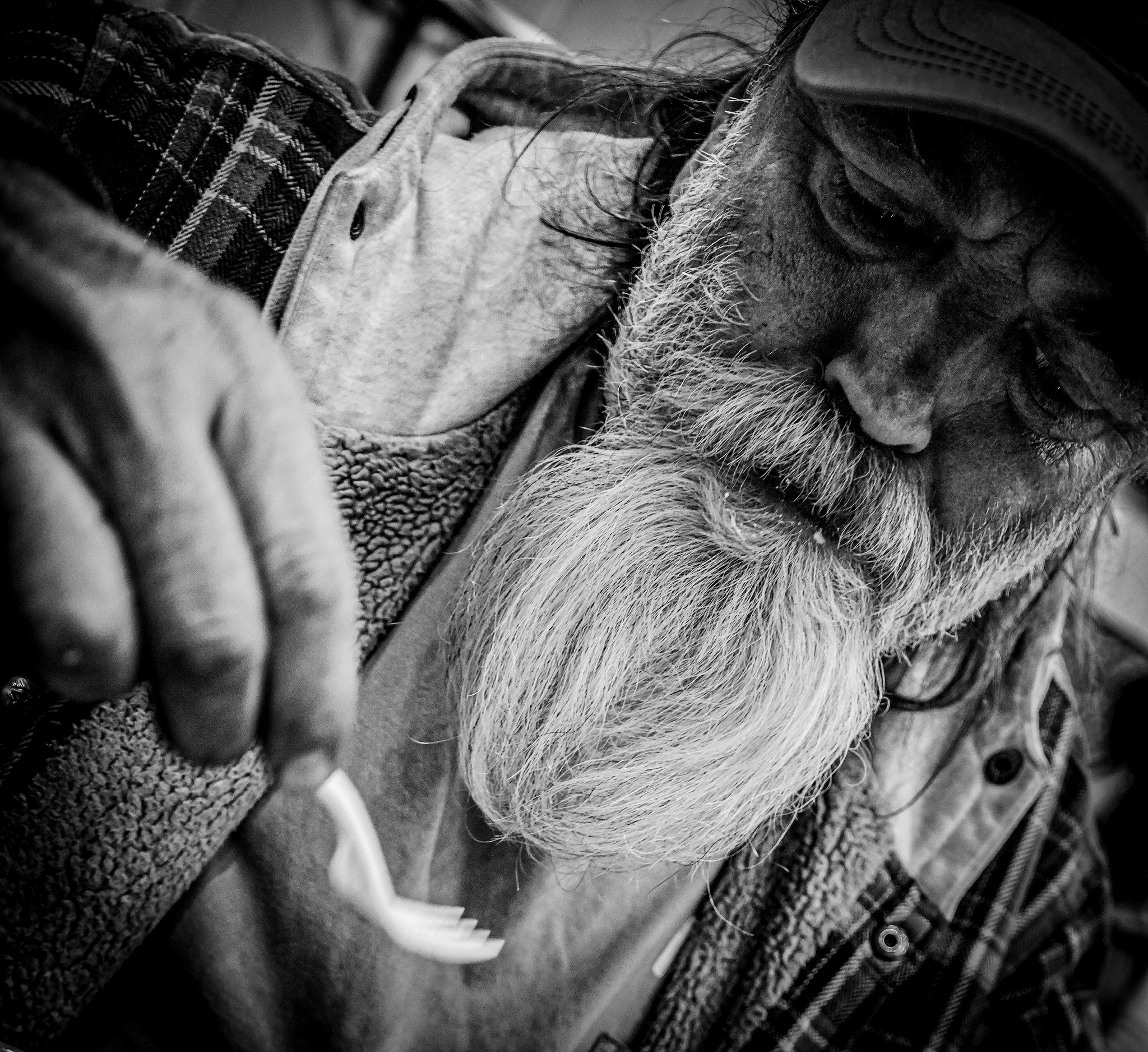 A bearded man with glasses and a cap, looking down, holding a fork, in black and white.