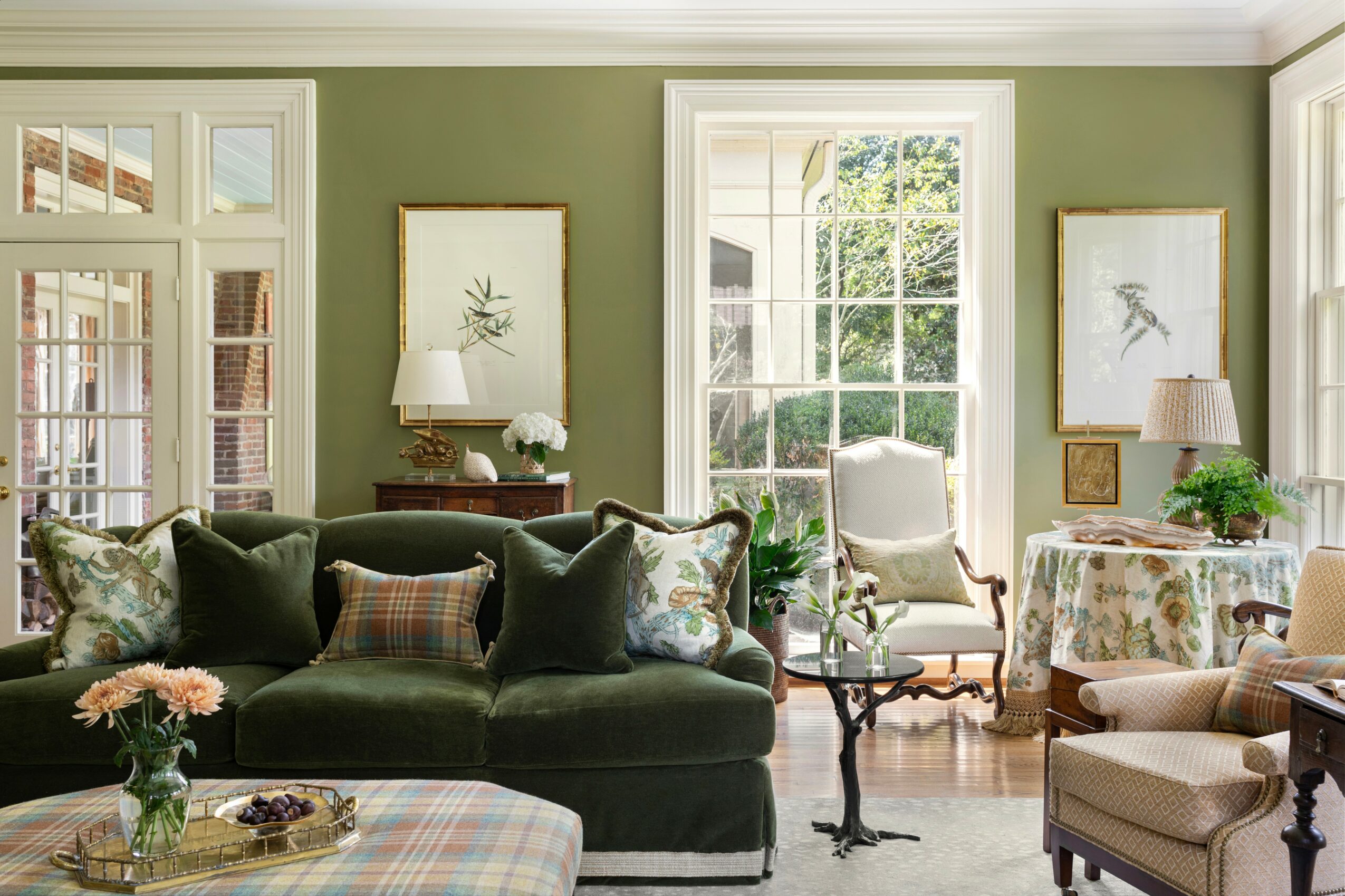 Living room with green walls, large windows, a dark green sofa with pillows, and a white armchair near a window.