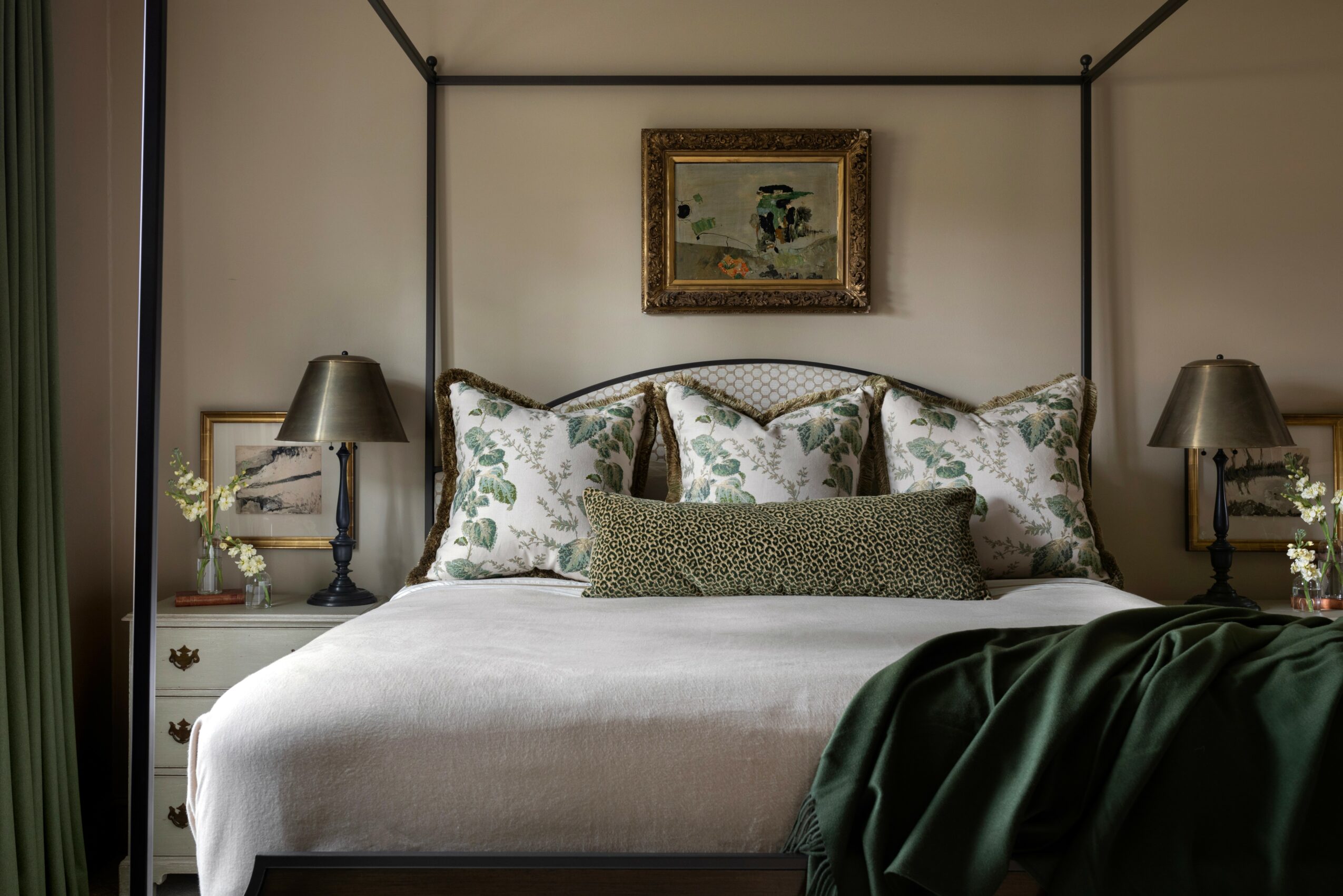 A bedroom with a bed, pillows, and a painting above, flanked by two nightstands with lamps, and a green curtain on the left.