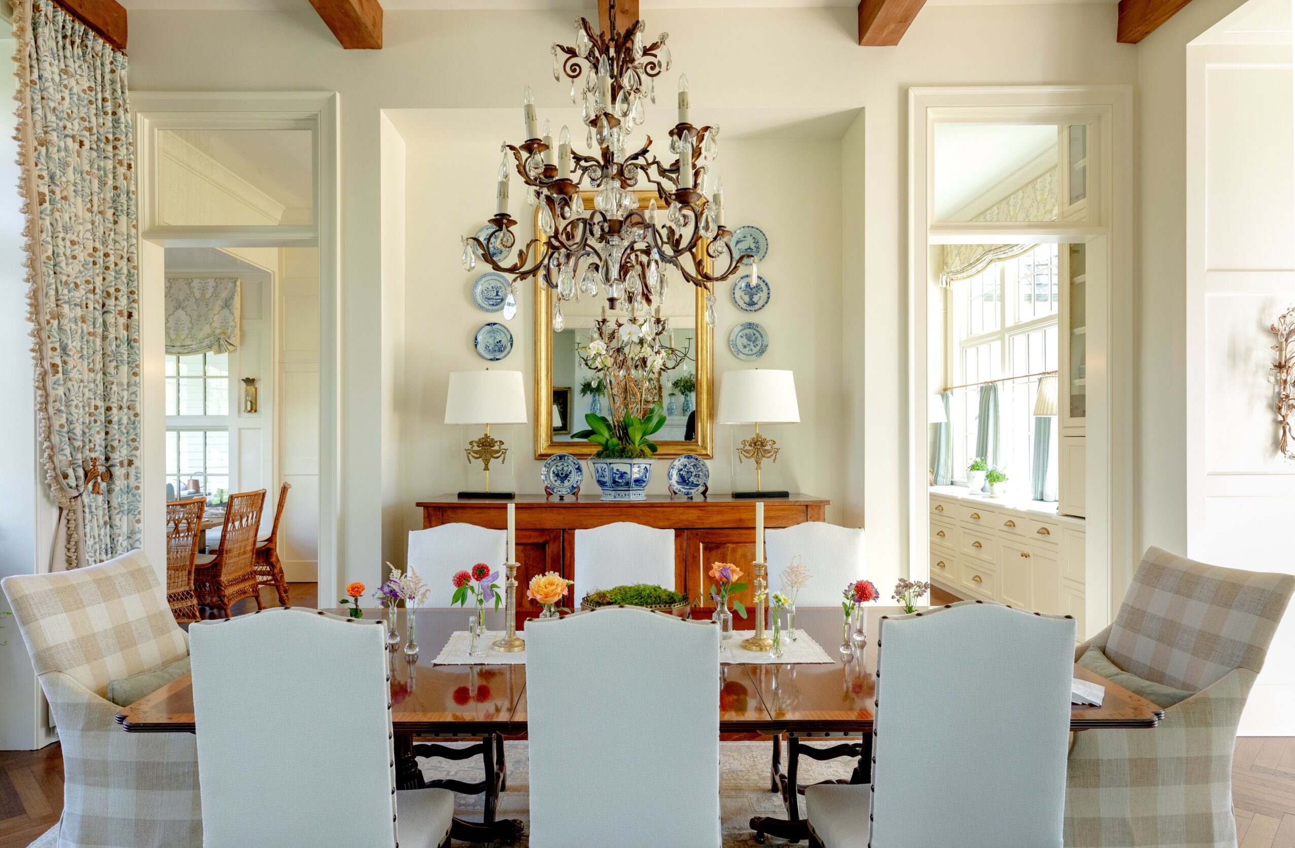 Dining room with a chandelier, mirror, wooden sideboard, and six chairs around a table, bright with natural light.