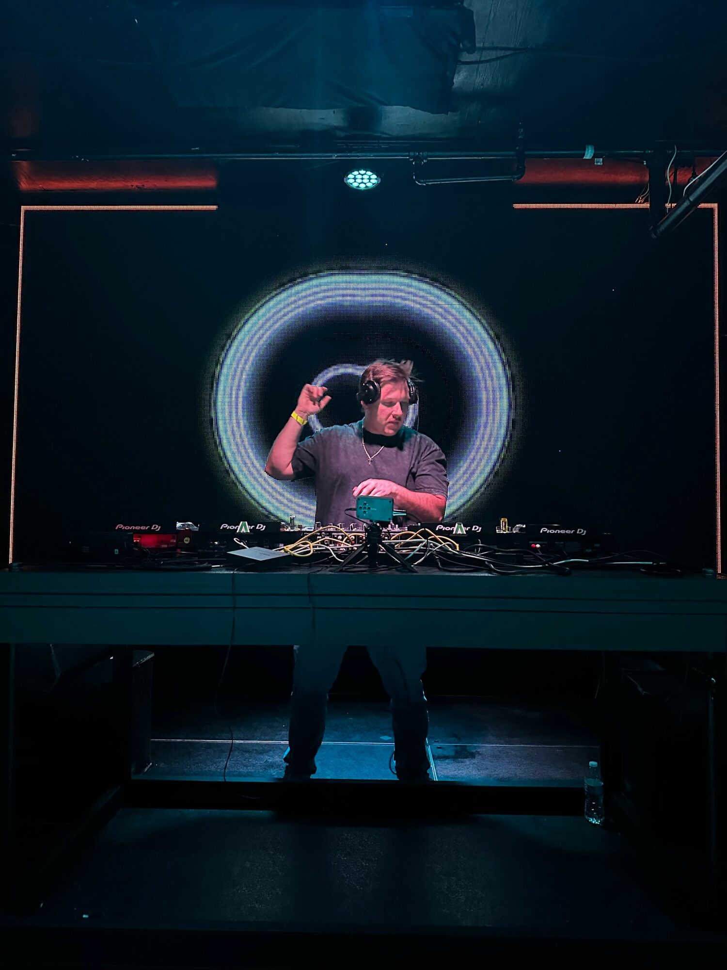 Person performing on stage with a circular light display behind, holding a microphone, in a dark setting.