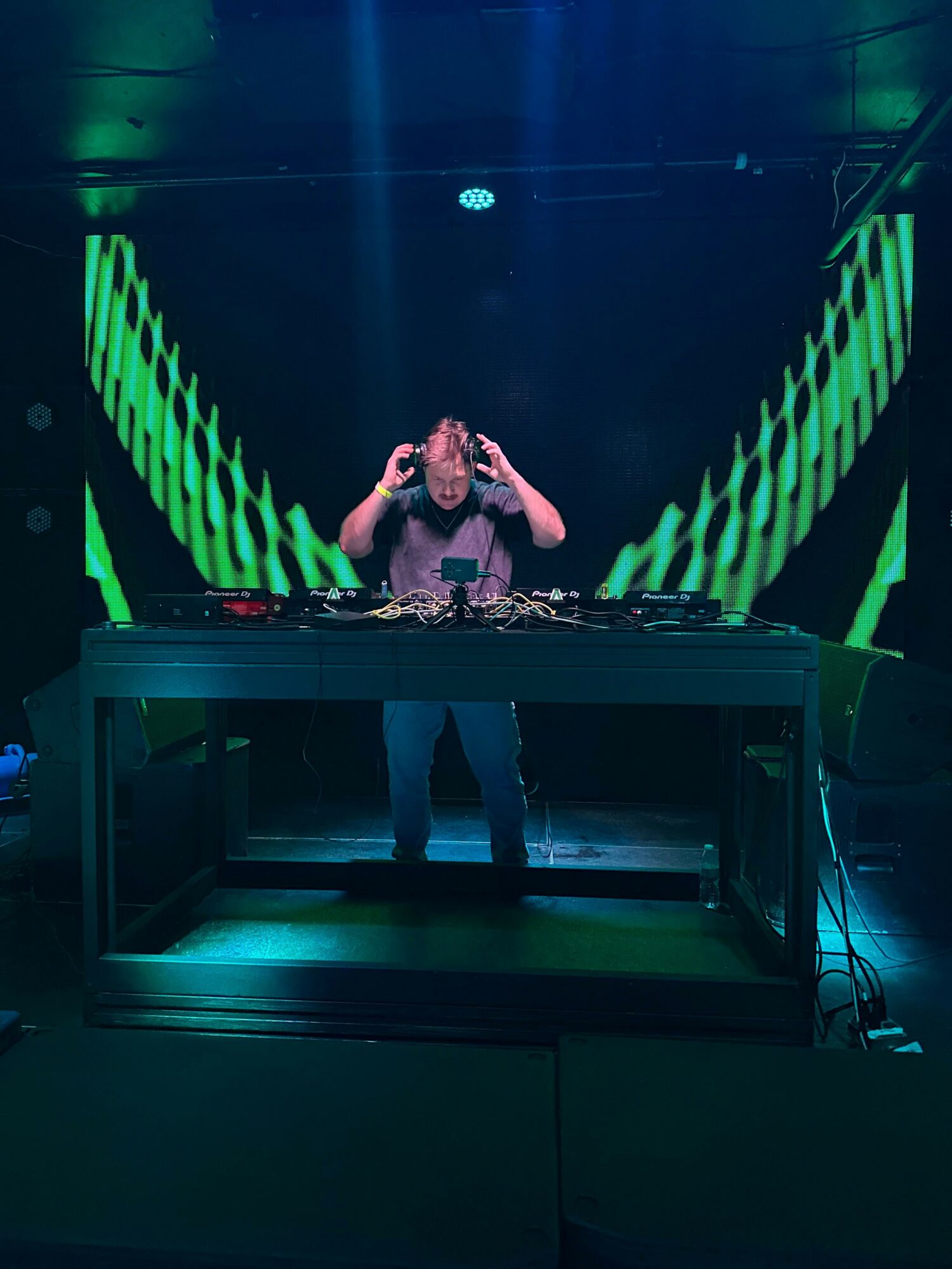 Person performing on stage with green and black lighting effects, standing on a platform, with stage equipment visible.