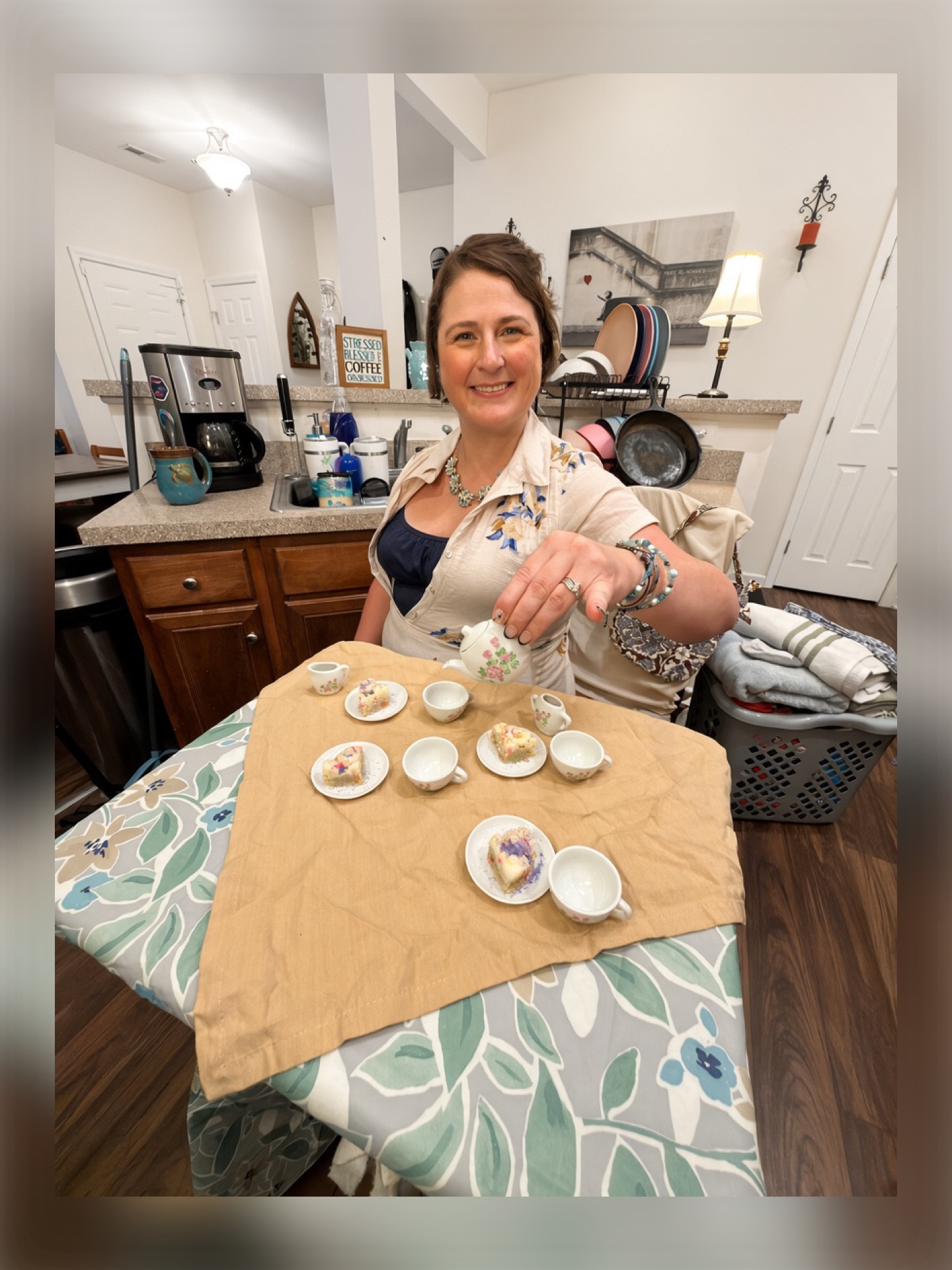 Woman smiling at camera with decorated cookies on table in kitchen, pouring milk into a cup, with various items in background.