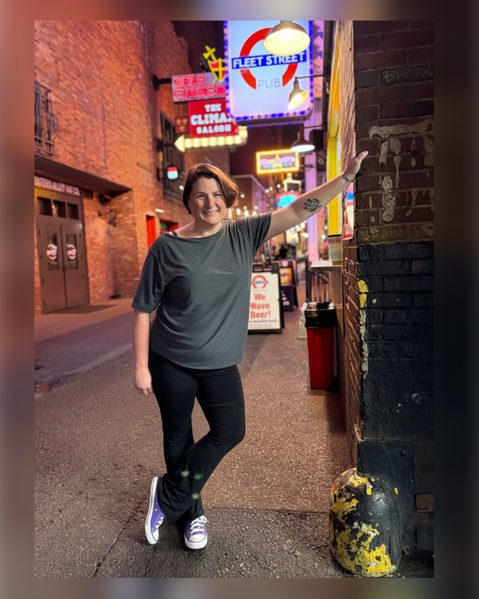 Woman standing on a city street at night, smiling, with colorful neon signs in the background.