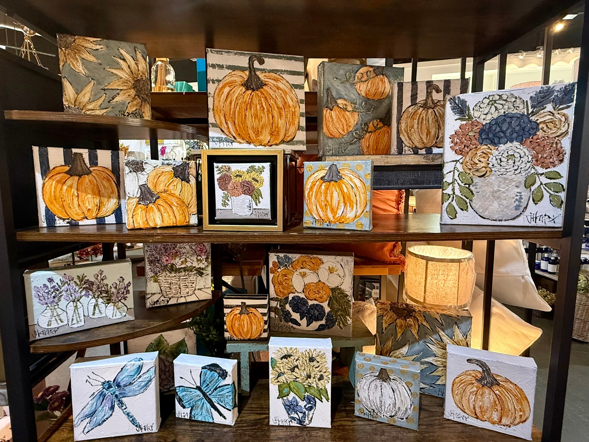 Shelves display various pumpkin-themed artwork and decorative items, including paintings, drawings, and a lamp, in a cozy indoor setting.