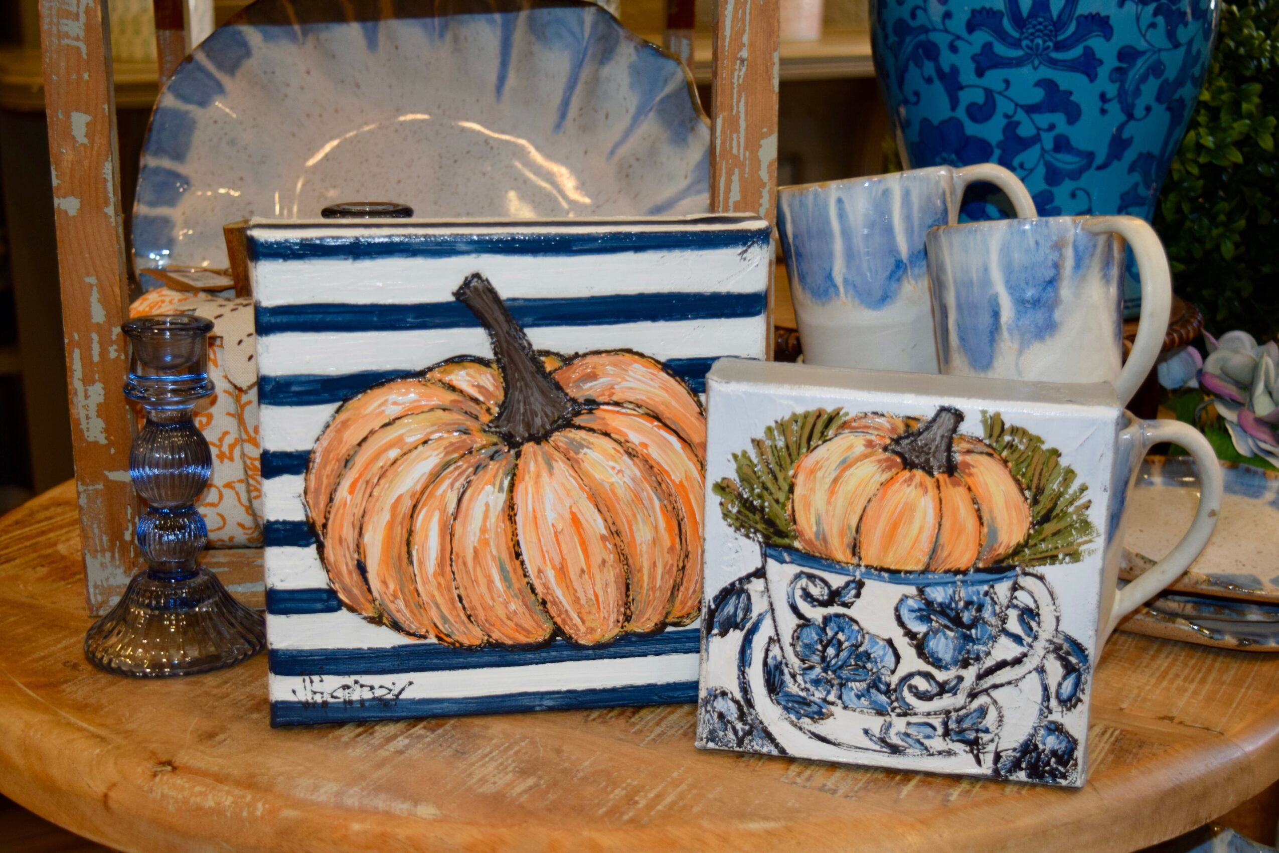 Pumpkin painted on a striped box, with a matching mug and a decorative tile, all on a wooden table.