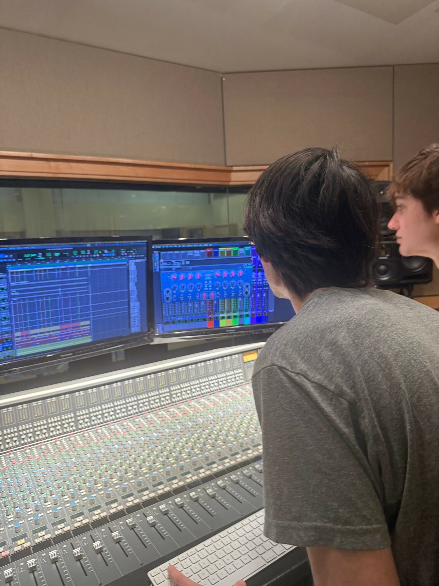 Two people working at a music mixing console with a computer screen displaying audio software.