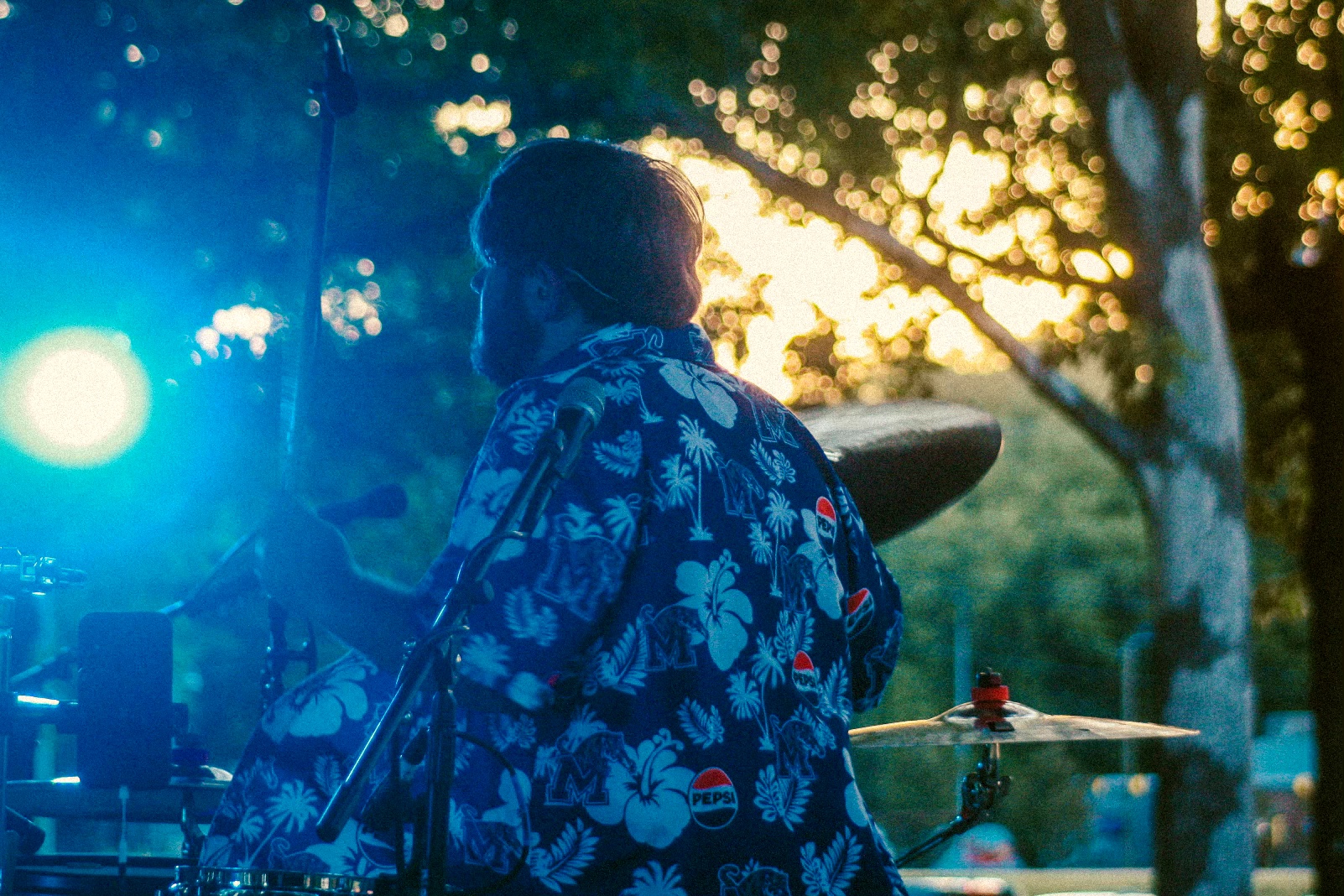 Person wearing a floral shirt outdoors with trees and sunlight in the background.