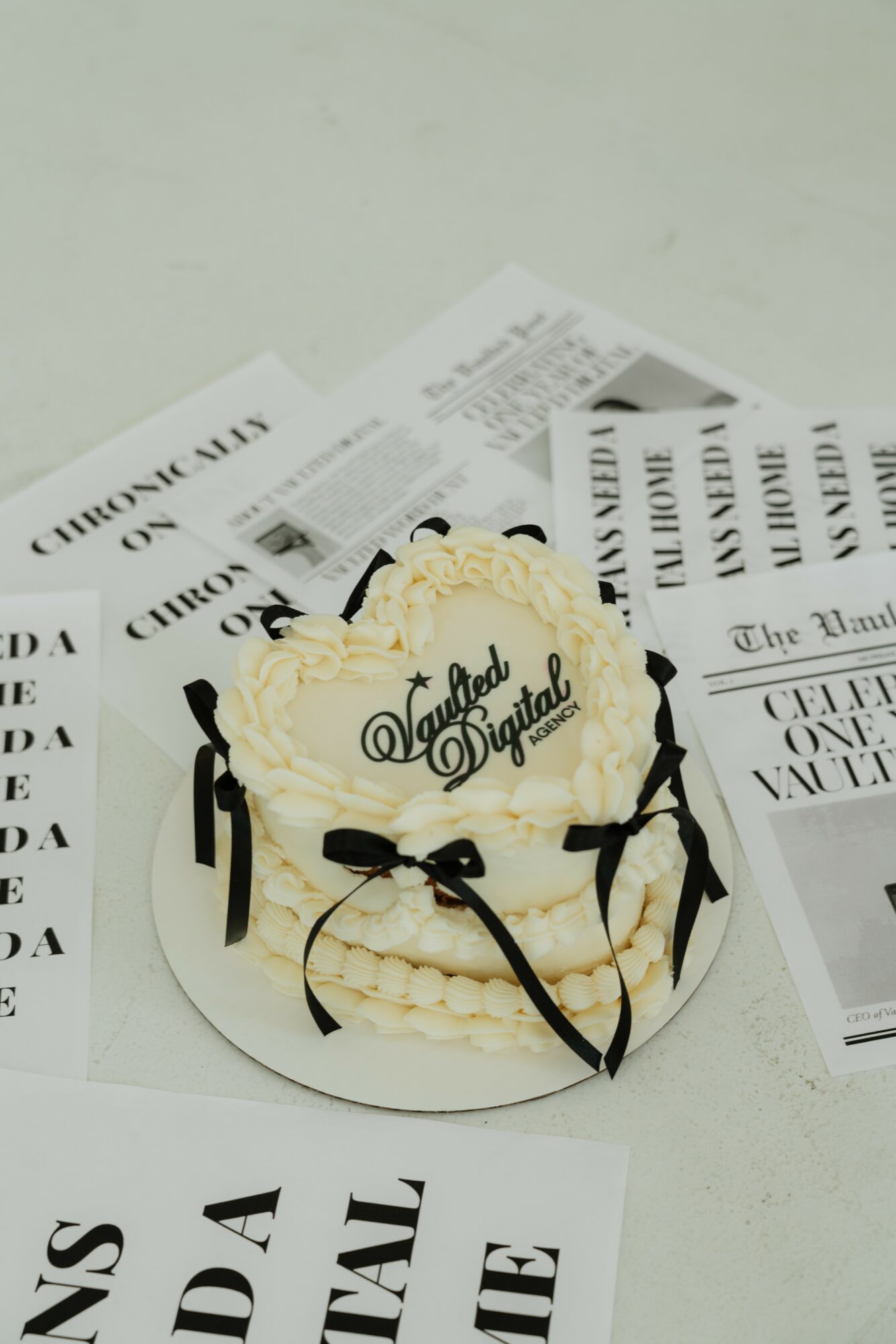 Round cake with white frosting, black ribbon decorations, and a sign that says